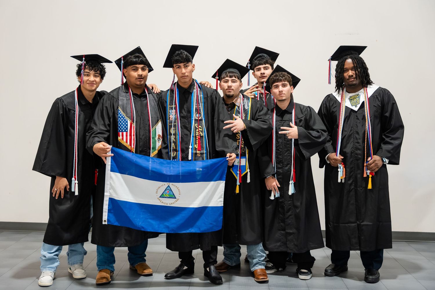 Group of graduates in black caps and gowns posing together, one holding a Nicaragua flag at a graduation ceremony.