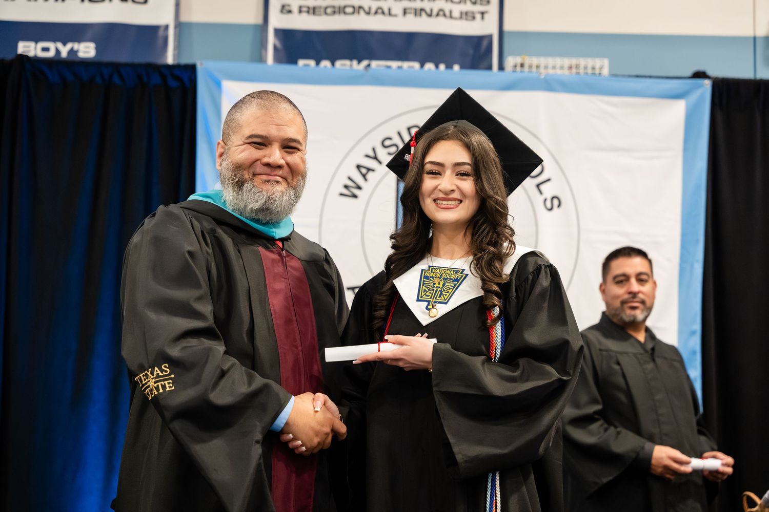 Graduate in cap and gown shakes hands with administrator at Wayside Schools graduation ceremony.