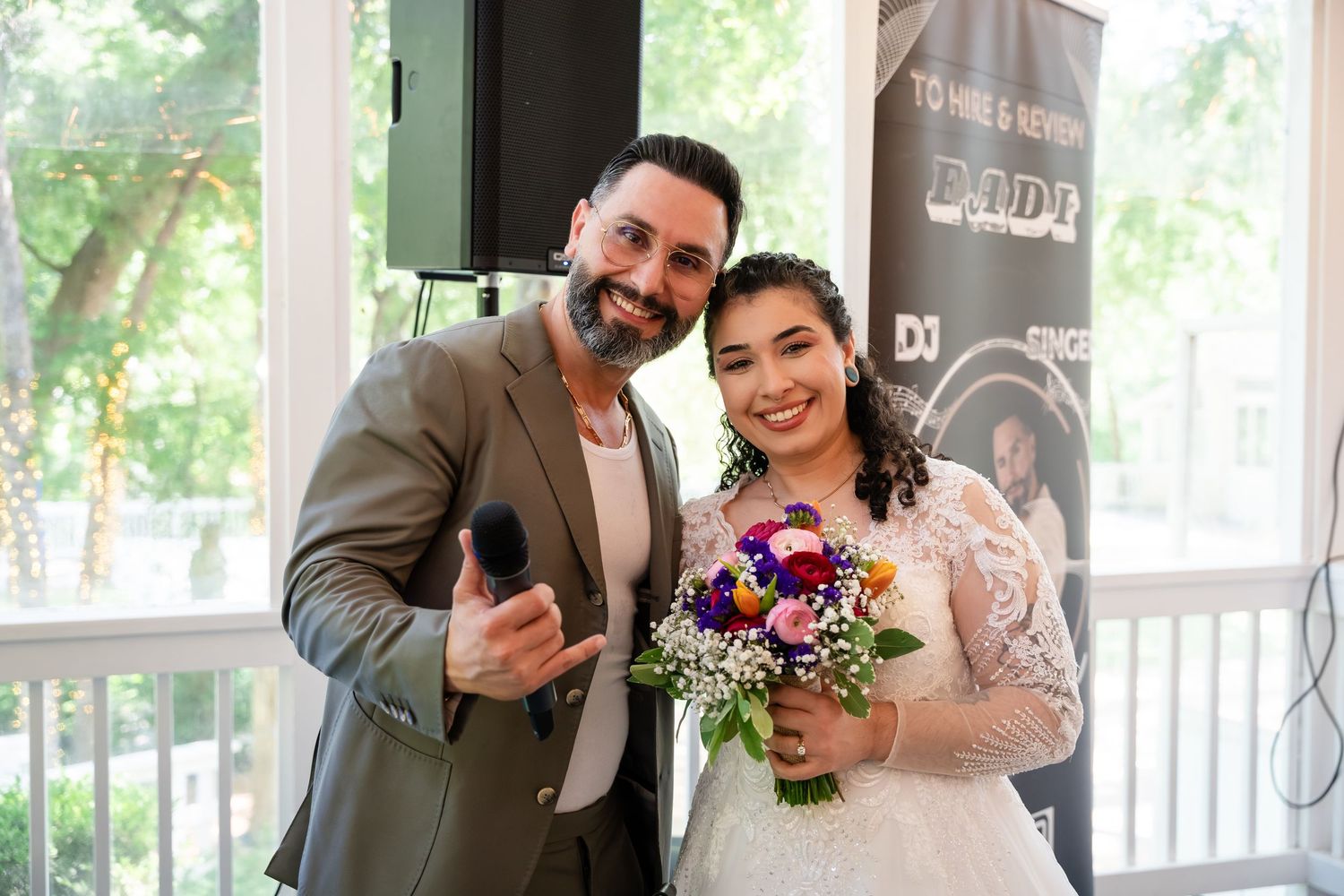 Smiling bride holding colorful bouquet poses with bearded groom in gray suit at elegant outdoor wedding reception.