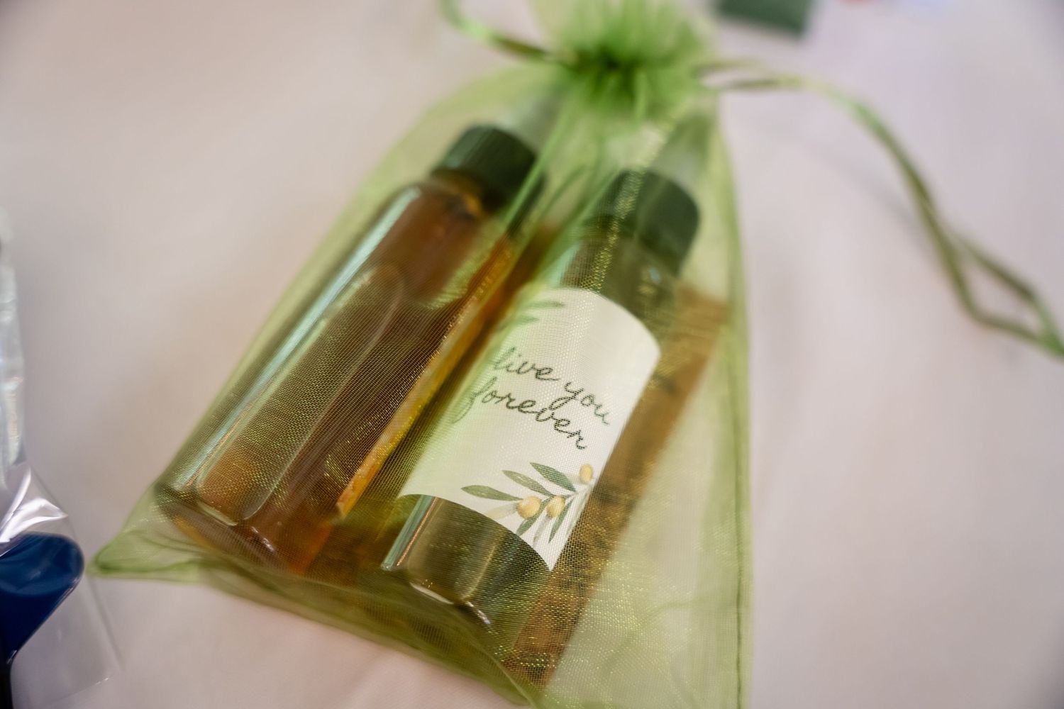 Green organza gift bag with two small bottles of olive oil labeled 'live you forever' wedding favor.