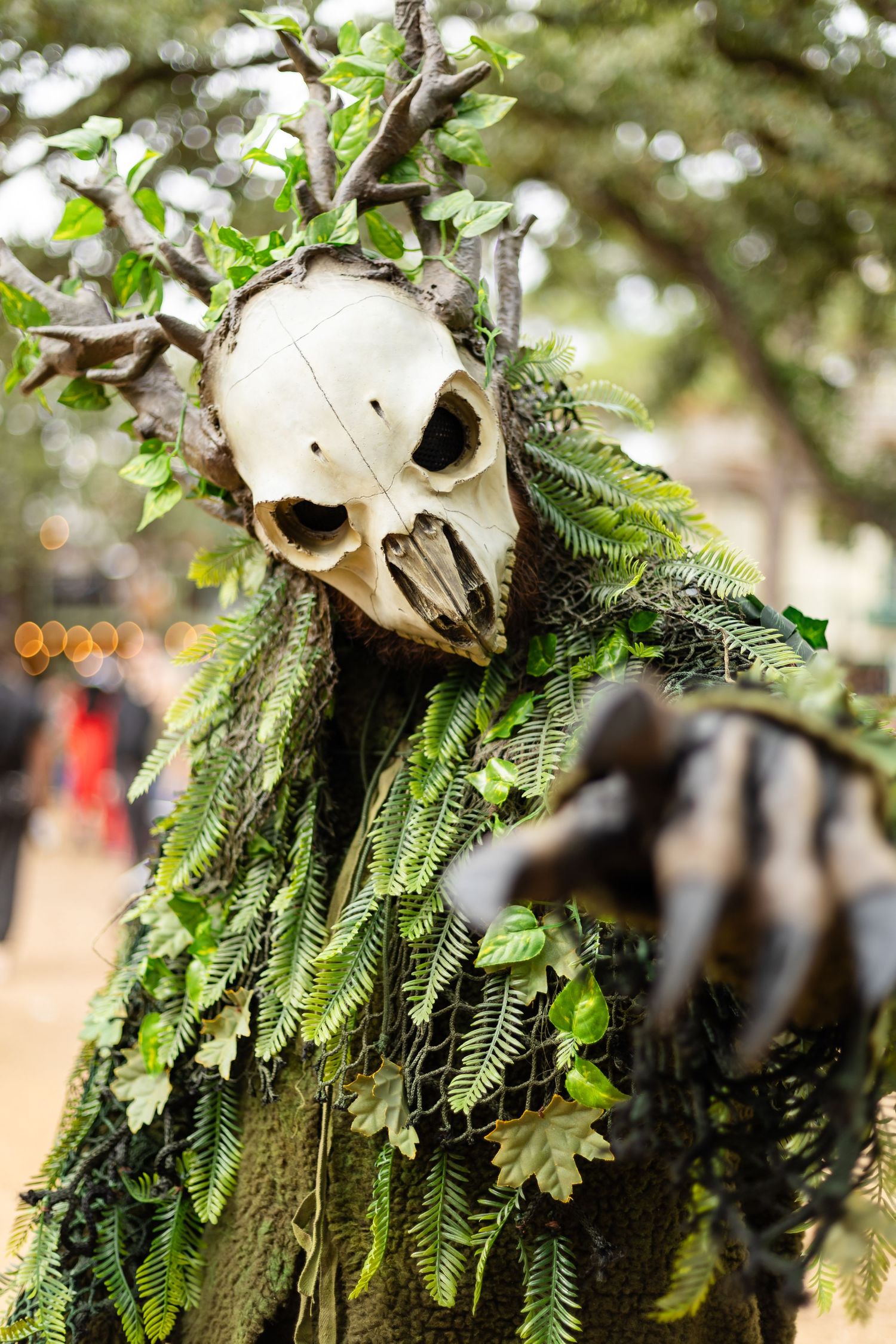 A spooky Halloween decoration featuring a skull adorned with green ferns and foliage against a blurred outdoor background.