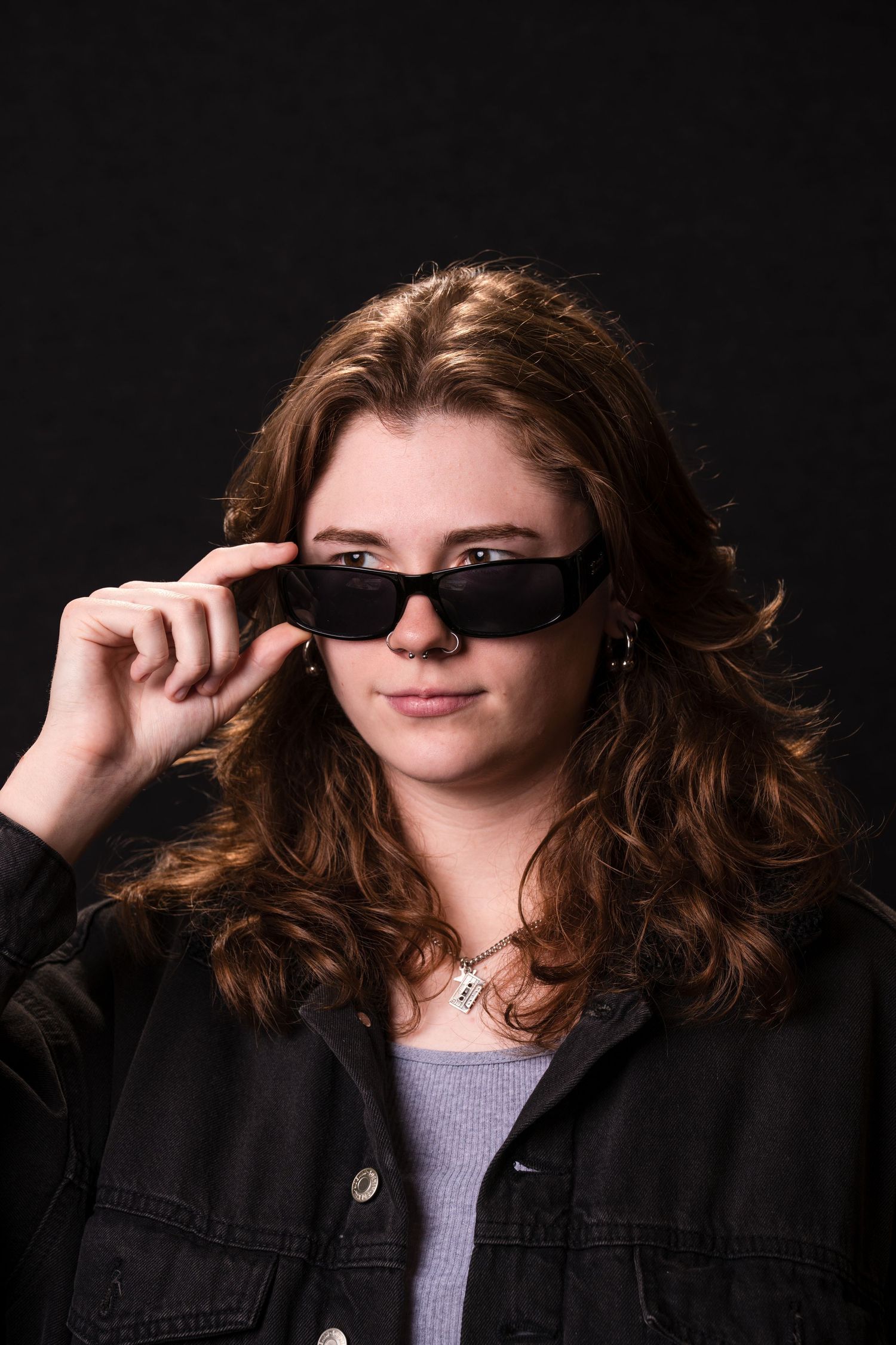 A person wearing sunglasses and a black jacket poses in a sequence showing them adjusting their glasses against dark background.