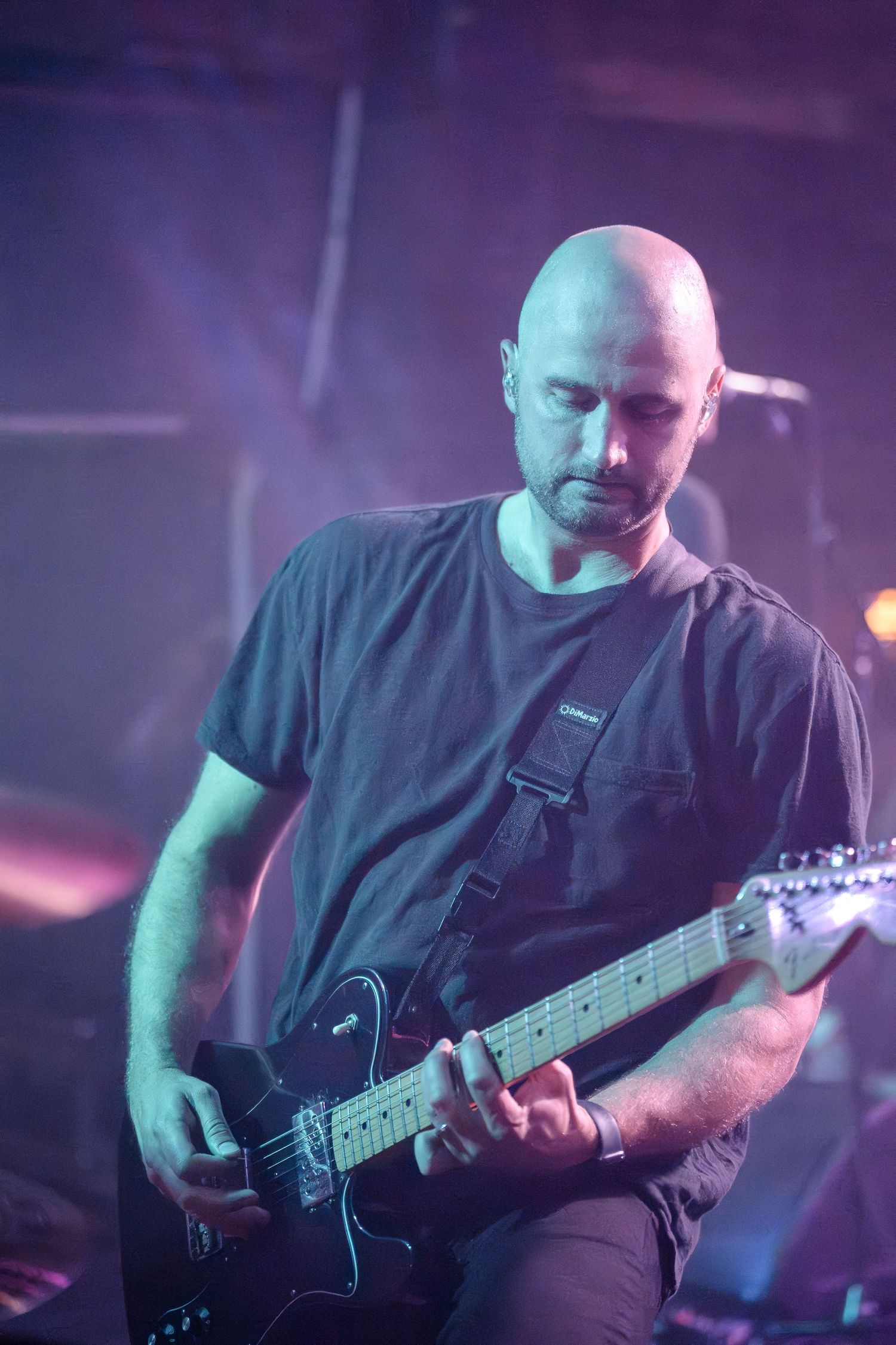 Guitarist plays electric guitar under dramatic purple stage lighting.