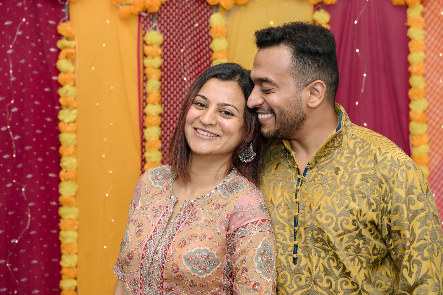 Couple in traditional Indian attire sharing a joyful moment against colorful backdrop.