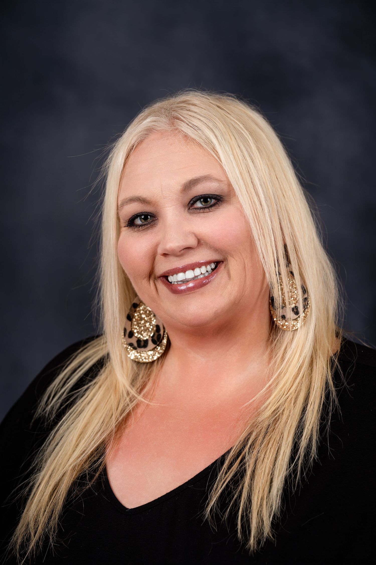 Professional portrait of person with long blonde hair wearing decorative gold earrings.