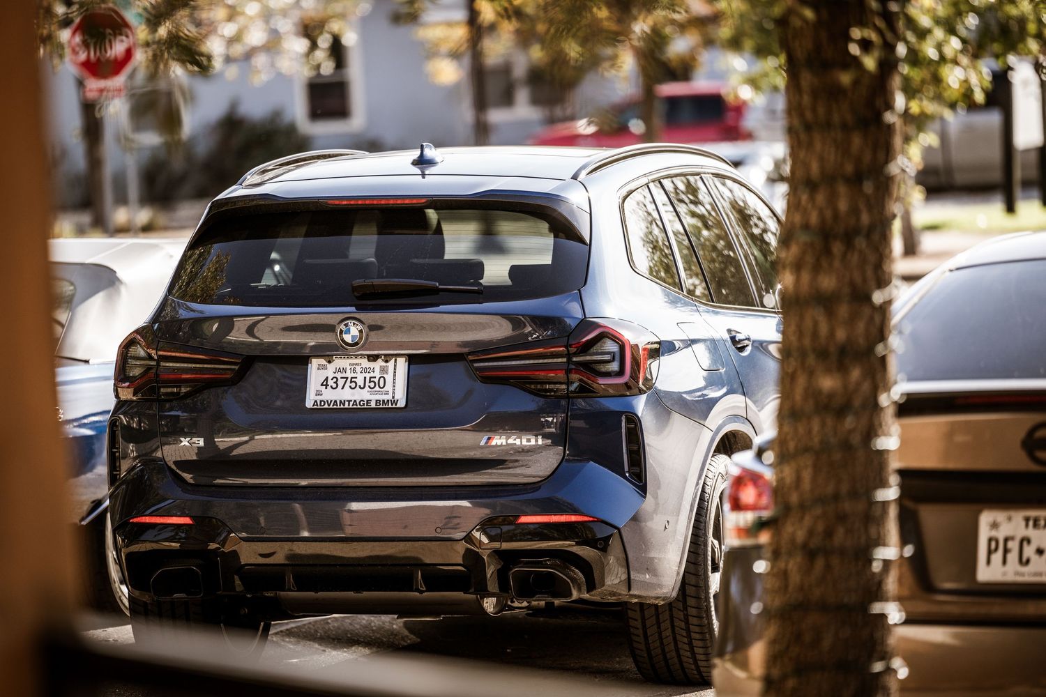 Rear view of a modern BMW X3 M40i SUV parked on a tree-lined street.