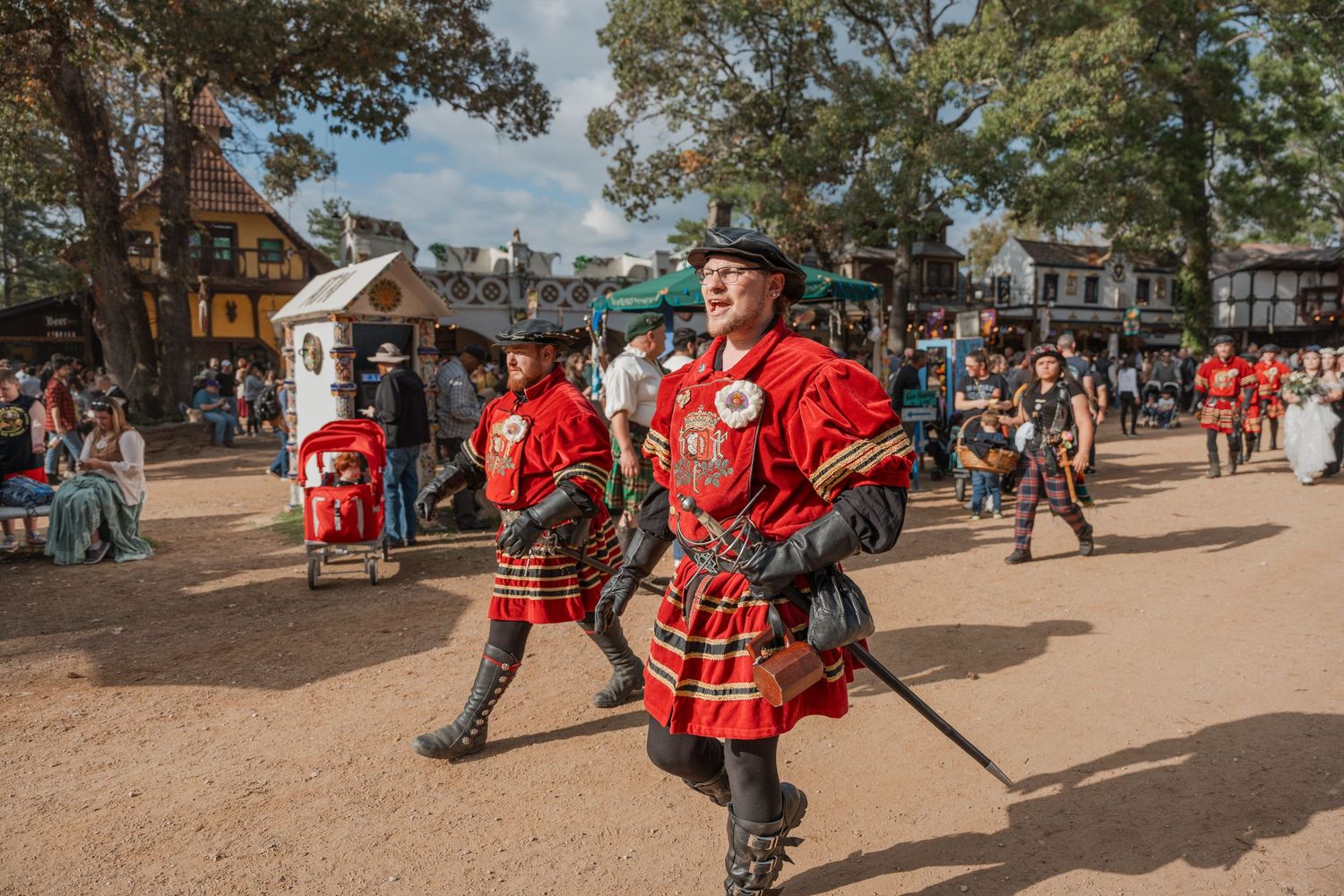Performers in red uniforms and kilts marching at a renaissance festival.