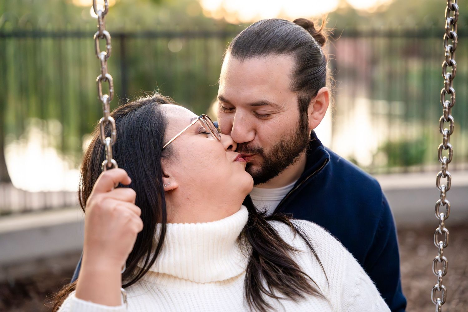 Couple sharing intimate moment on swing set during golden hour.
