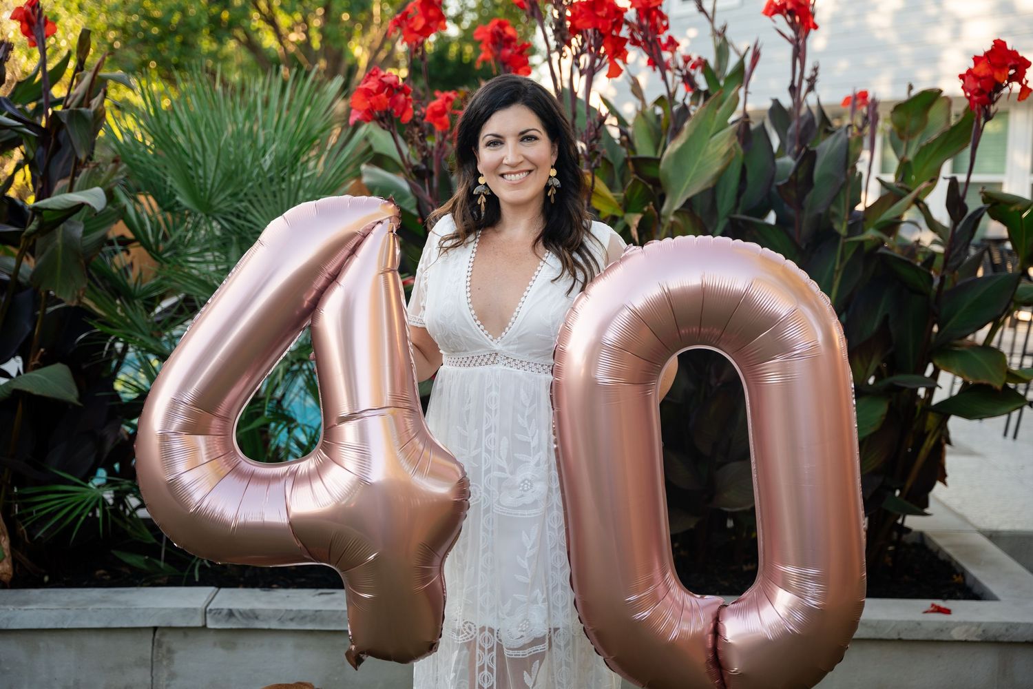 Rose gold number 40 balloons against a backdrop of red flowers and tropical plants.