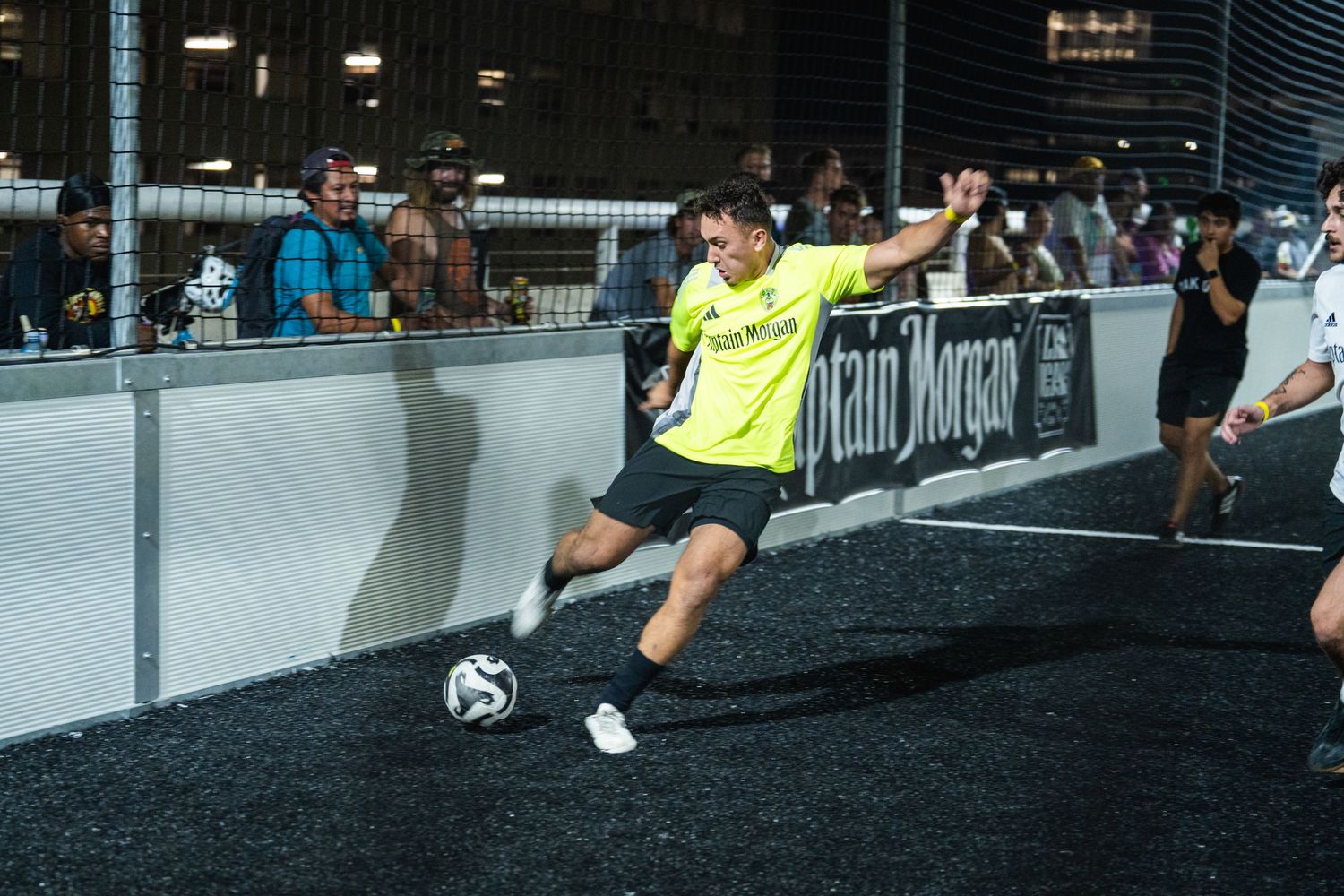 Player in bright yellow uniform kicks soccer ball near boundary wall during indoor match.