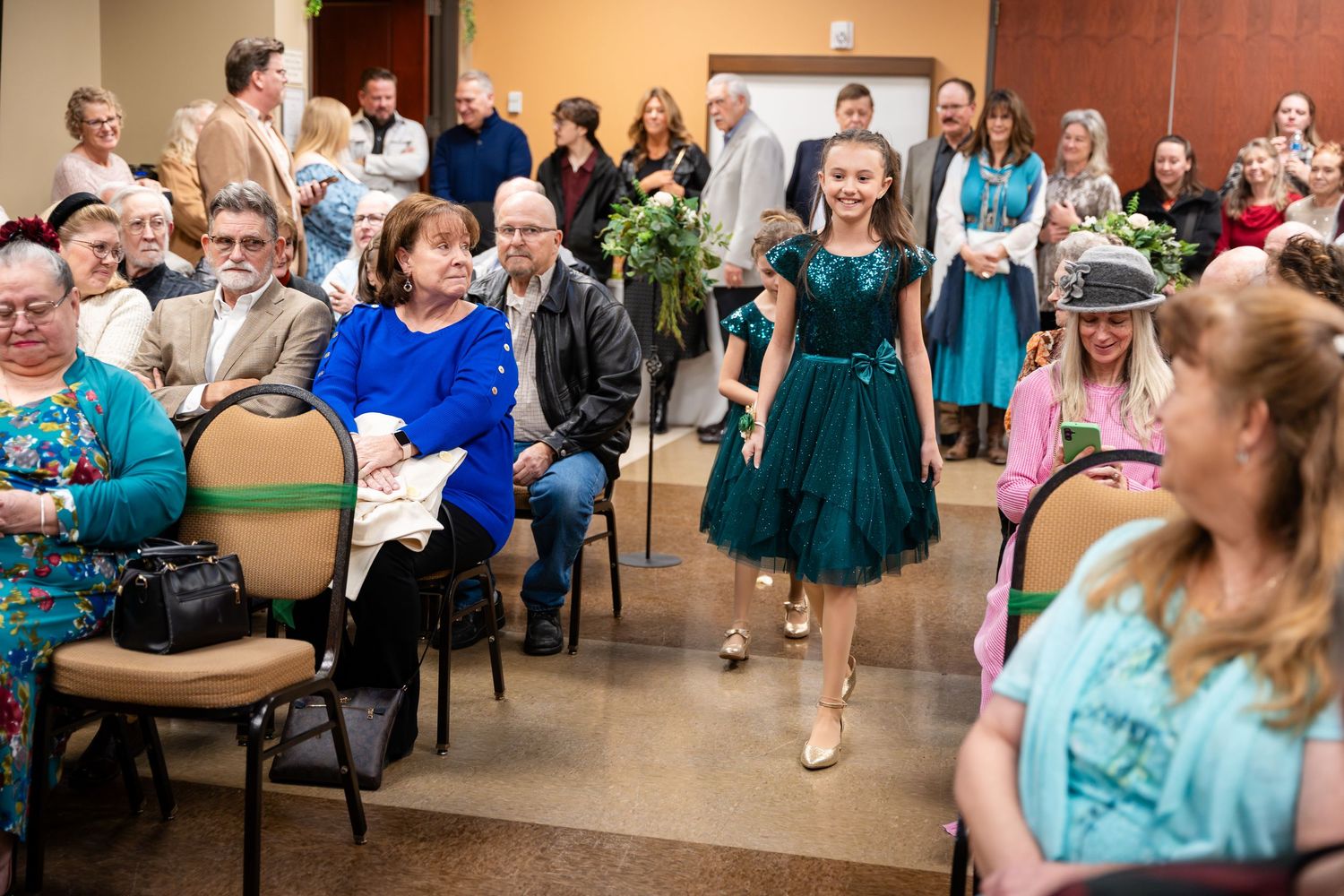 Guests sit and stand in a reception hall with people wearing coordinated blue and turquoise outfits.