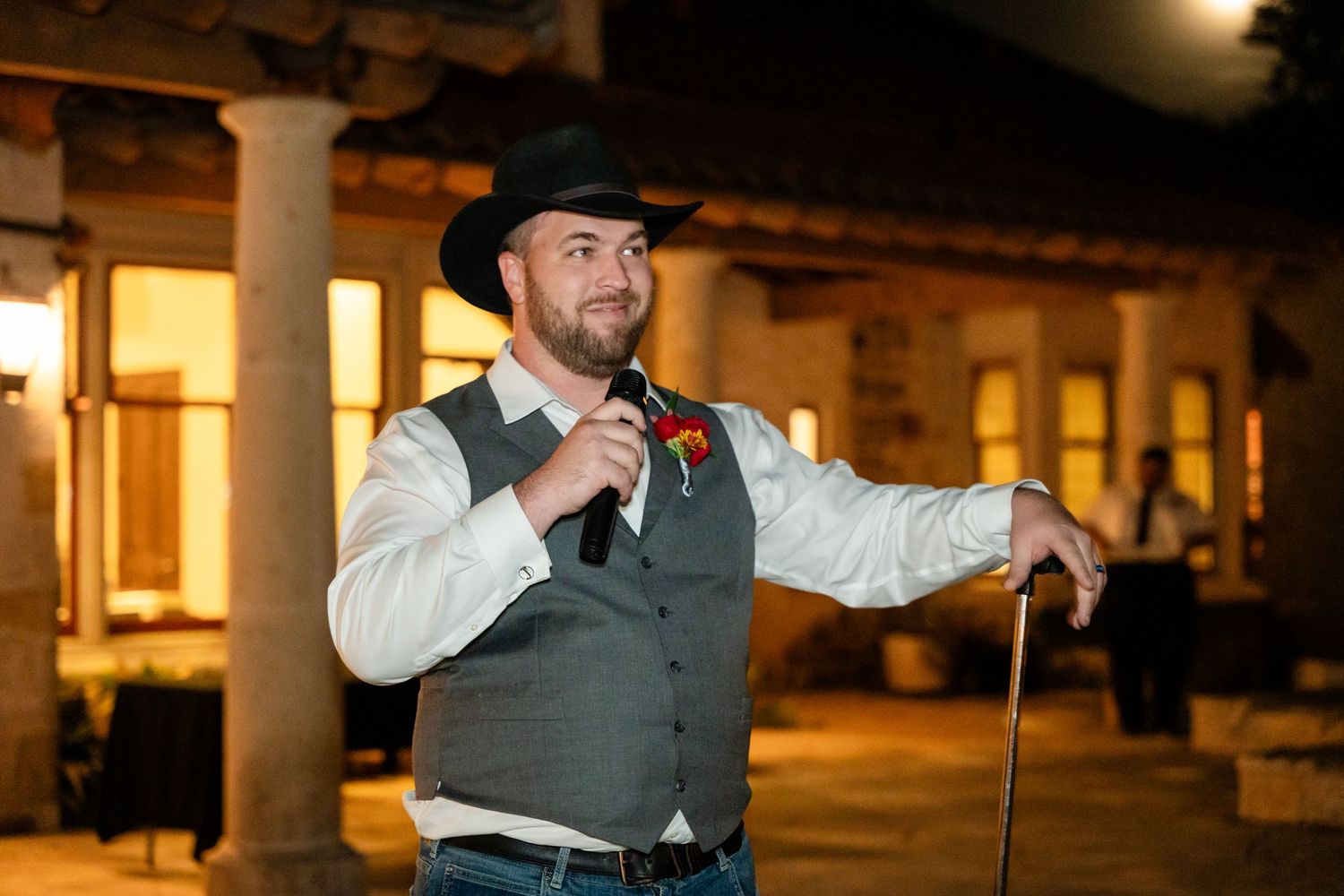 Person in western attire speaking into microphone at outdoor evening event.
