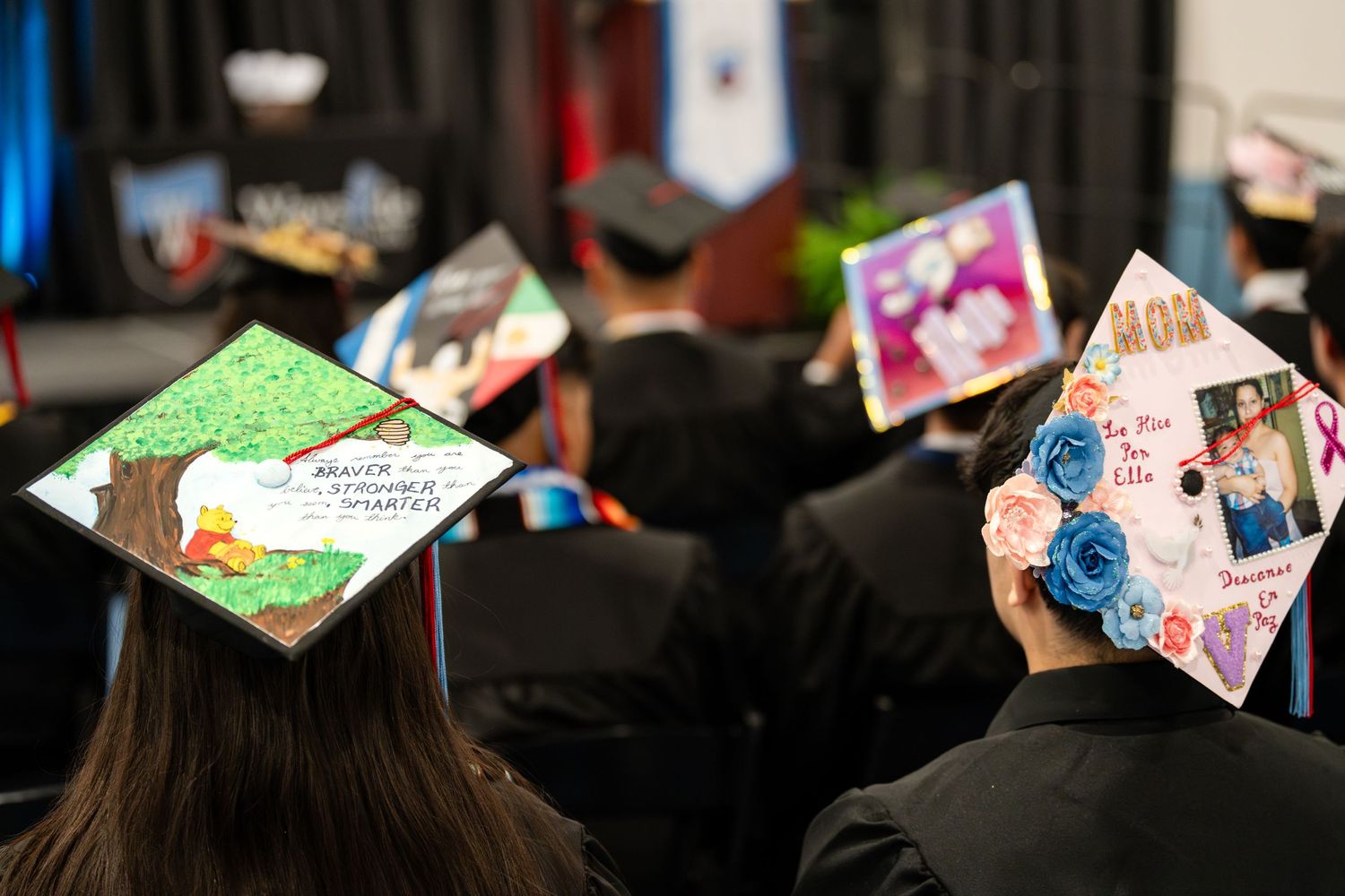 Decorated graduation caps with colorful designs seen from behind during commencement ceremony.