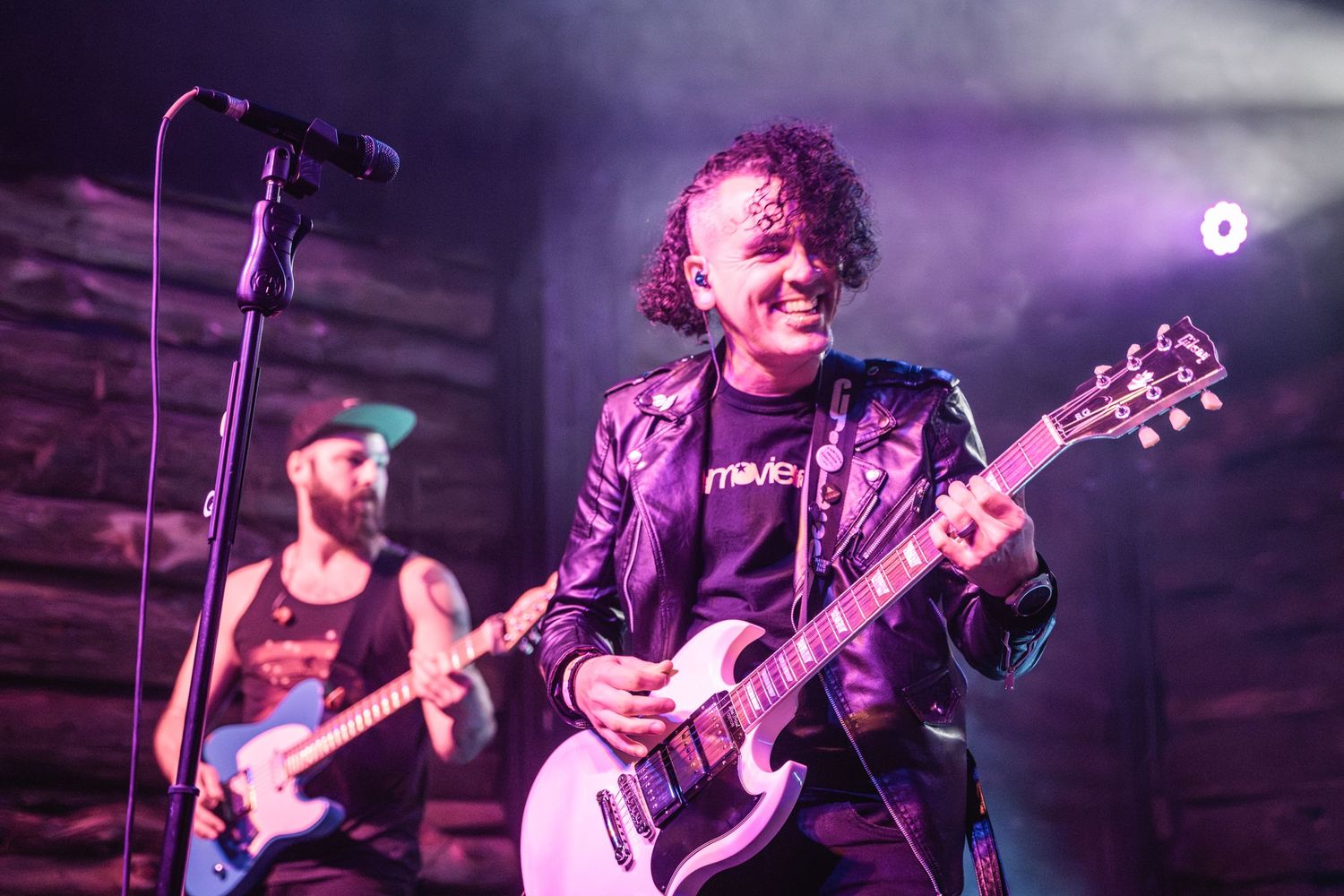 Musicians performing on stage with colorful purple lighting effects.