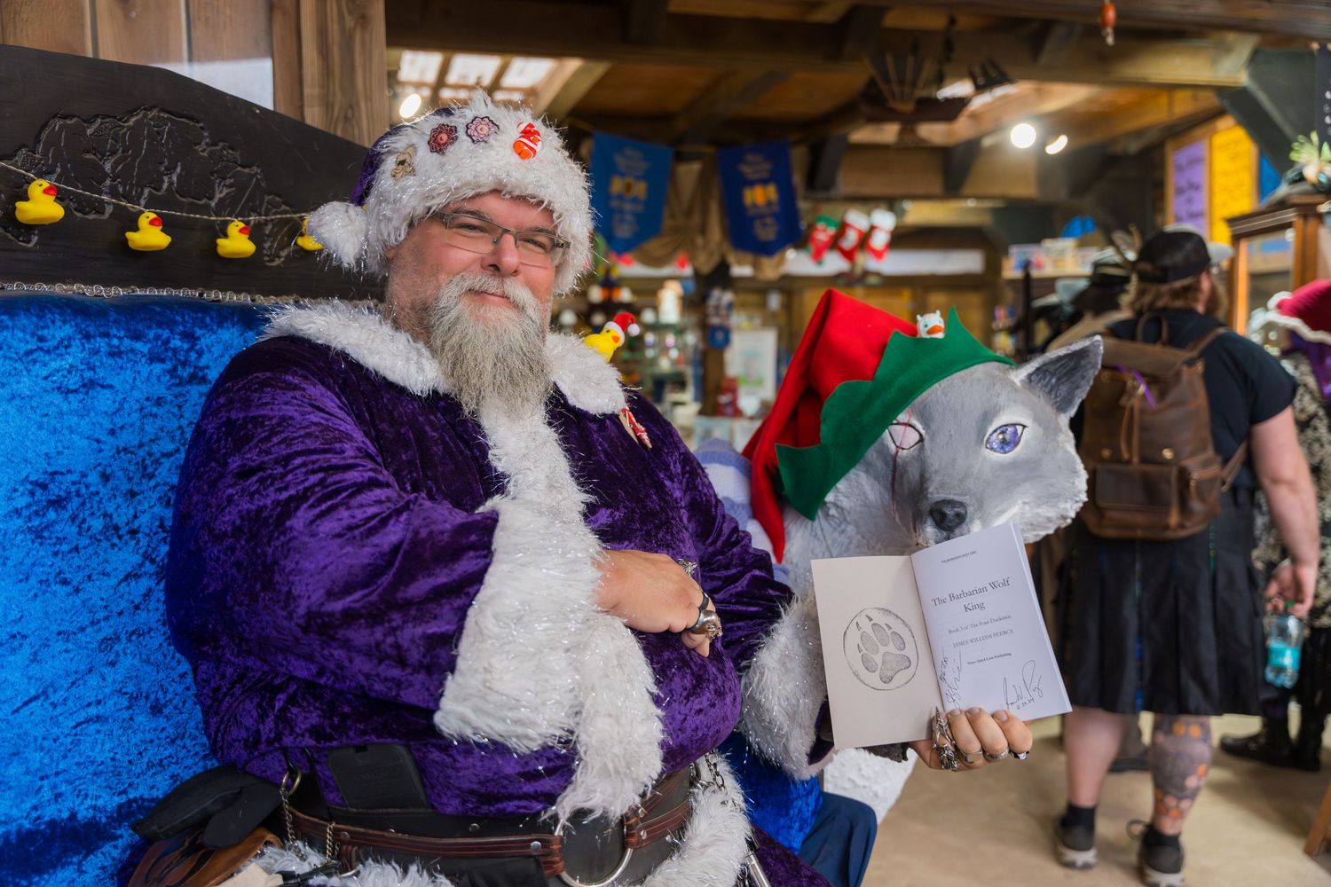 A festively dressed performer in purple and white sits on a decorated throne.