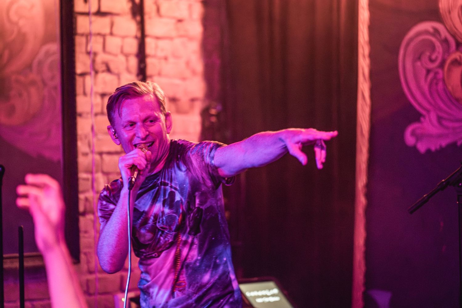 A performer points while singing on stage illuminated by purple lighting.