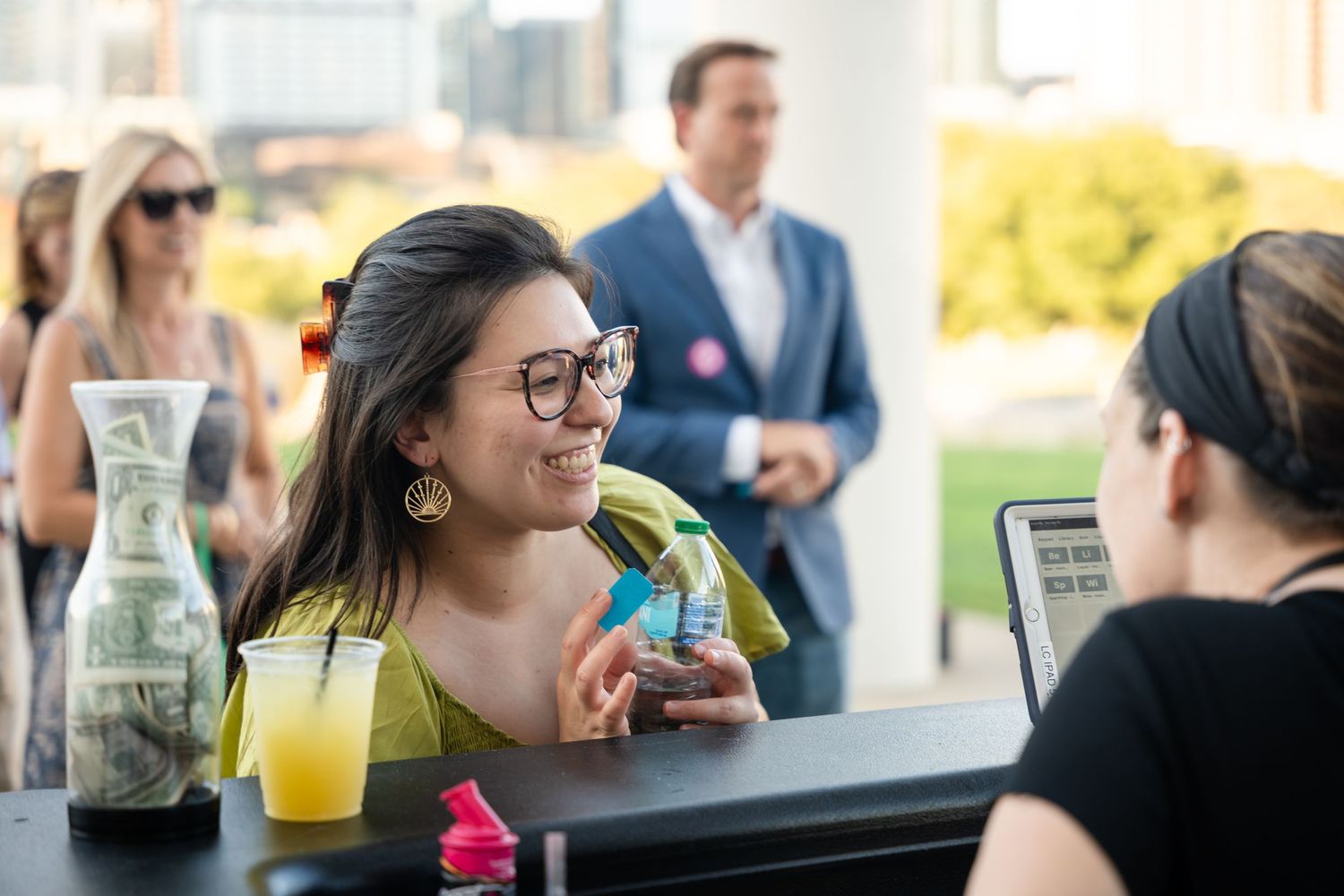 Customer ordering drinks at outdoor festival bar counter with city skyline visible.