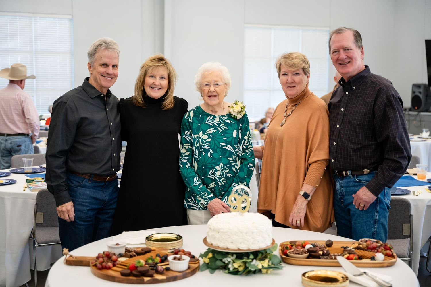 People stand behind a table of food displays at an indoor social event.