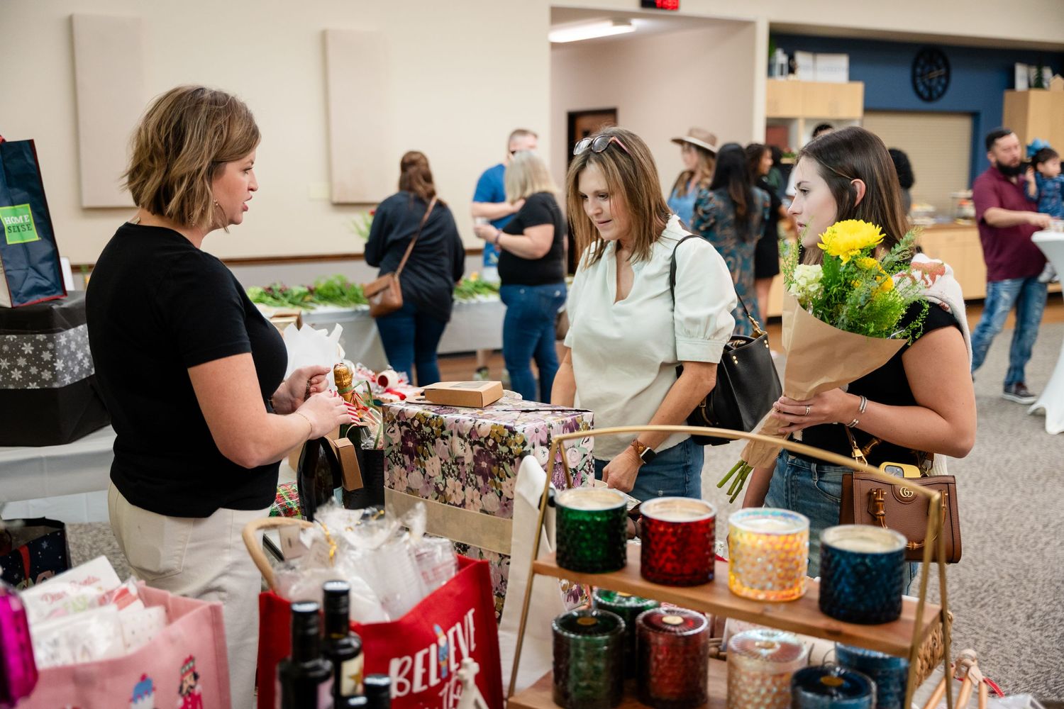 Shoppers browsing merchandise at a craft fair with various items on display.