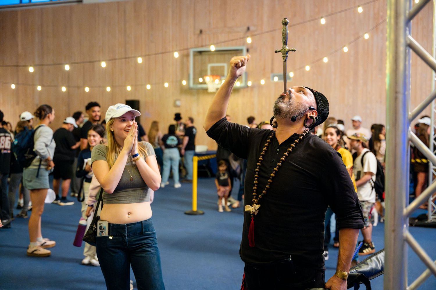 People react excitedly beneath strings of lights at an indoor event with metal scaffolding visible.
