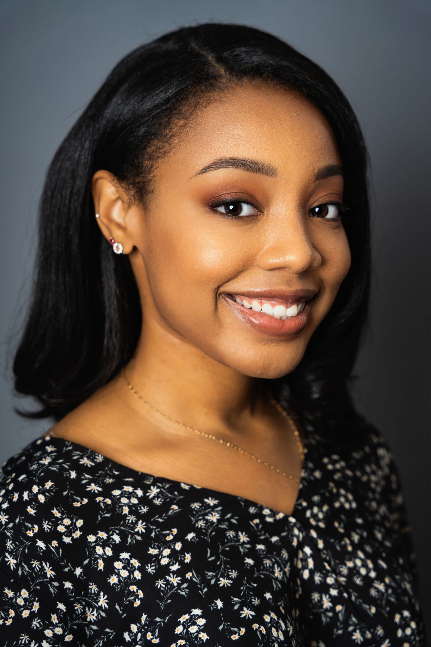 Professional headshot showing bright smile and floral print top against studio lighting.