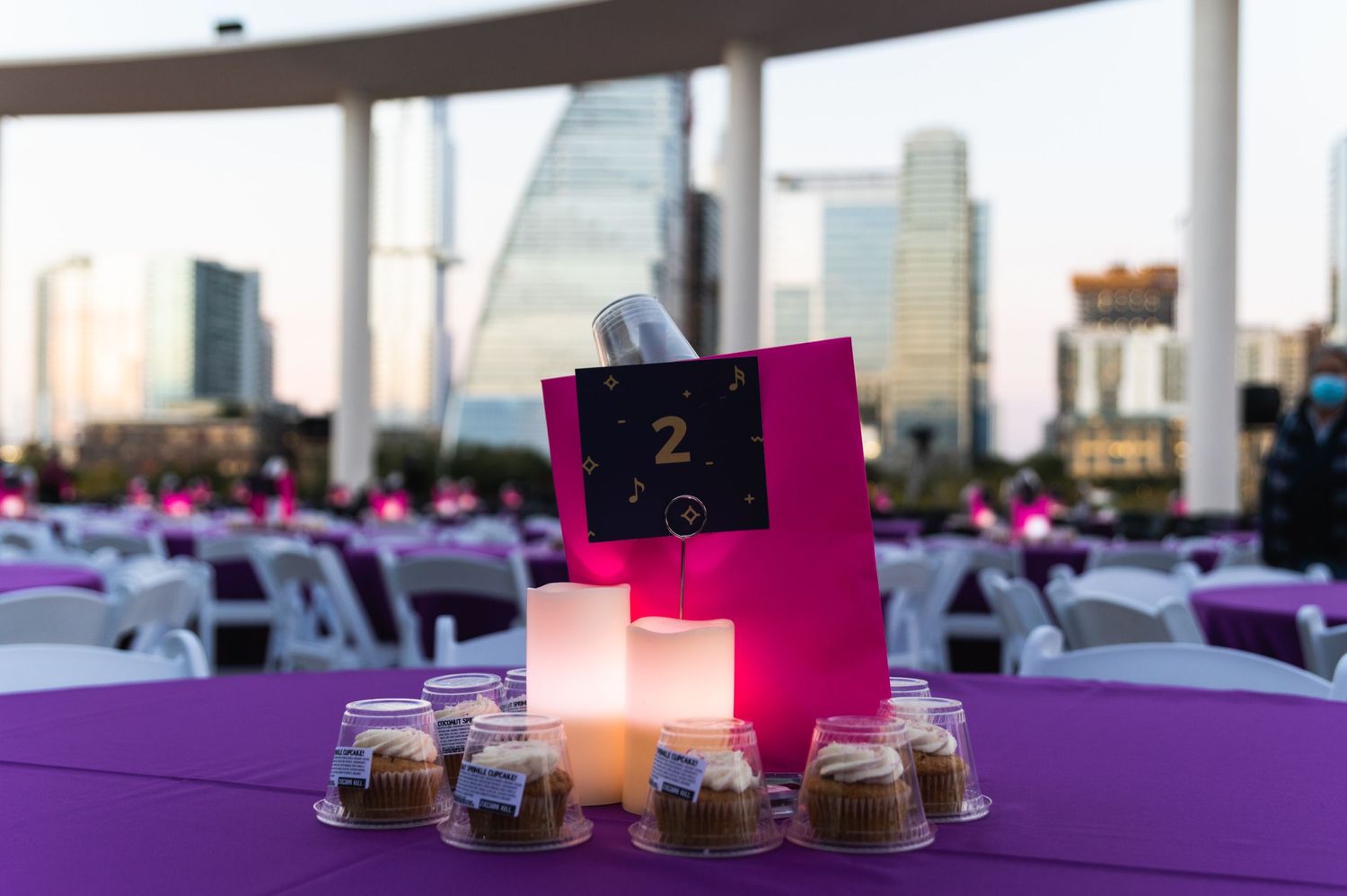 Table setting with pink centerpiece, candle and table number against city skyline backdrop.