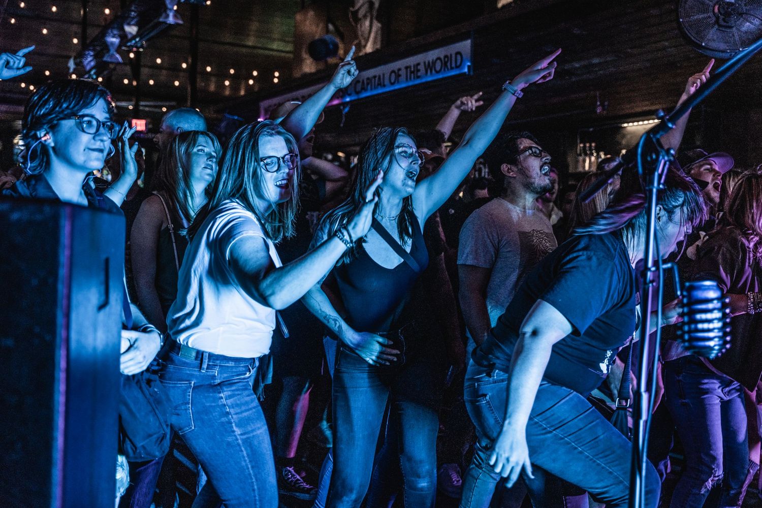 Energetic crowd at a nightclub illuminated in blue light dancing with raised arms during a live performance.