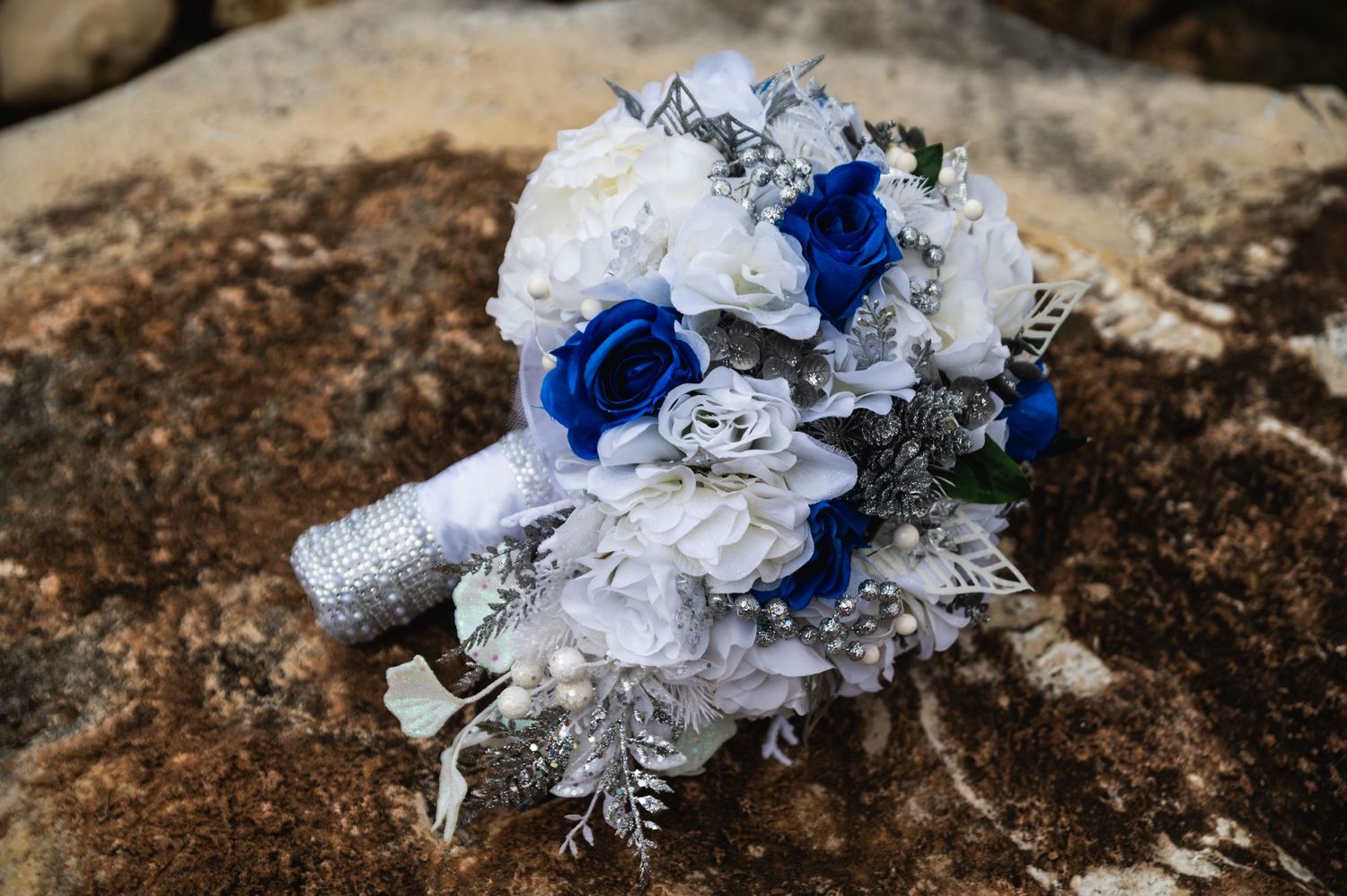 A bridal bouquet featuring white and blue roses with silver accents.