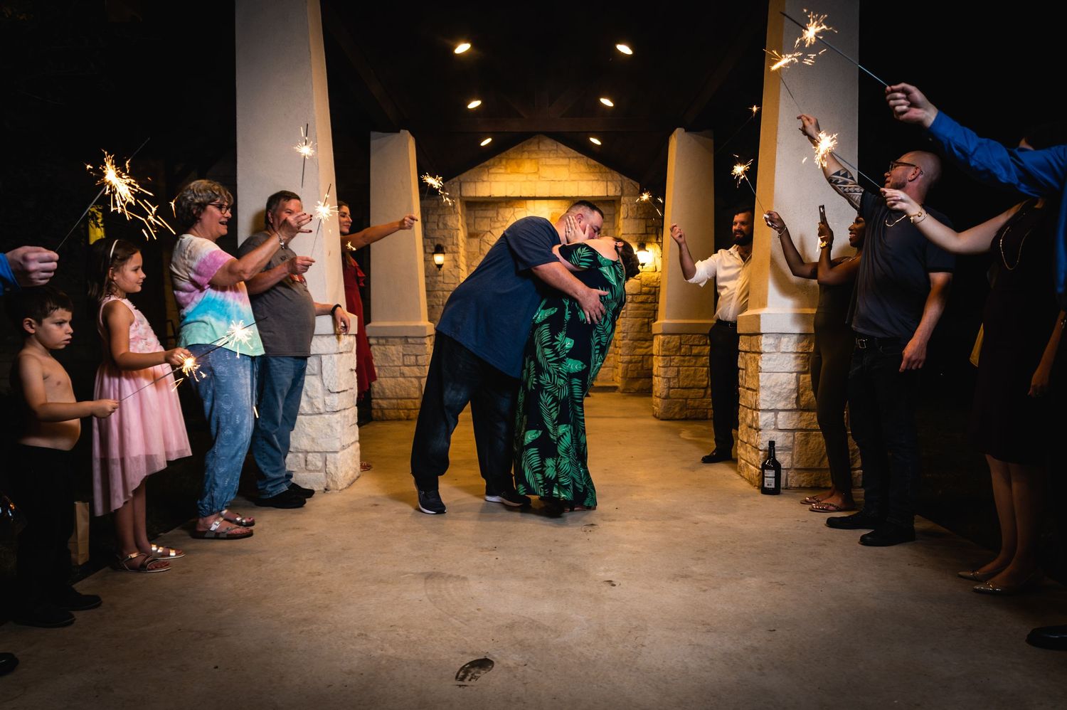 Sparklers create a magical exit tunnel for a dancing couple in a dimly lit venue.