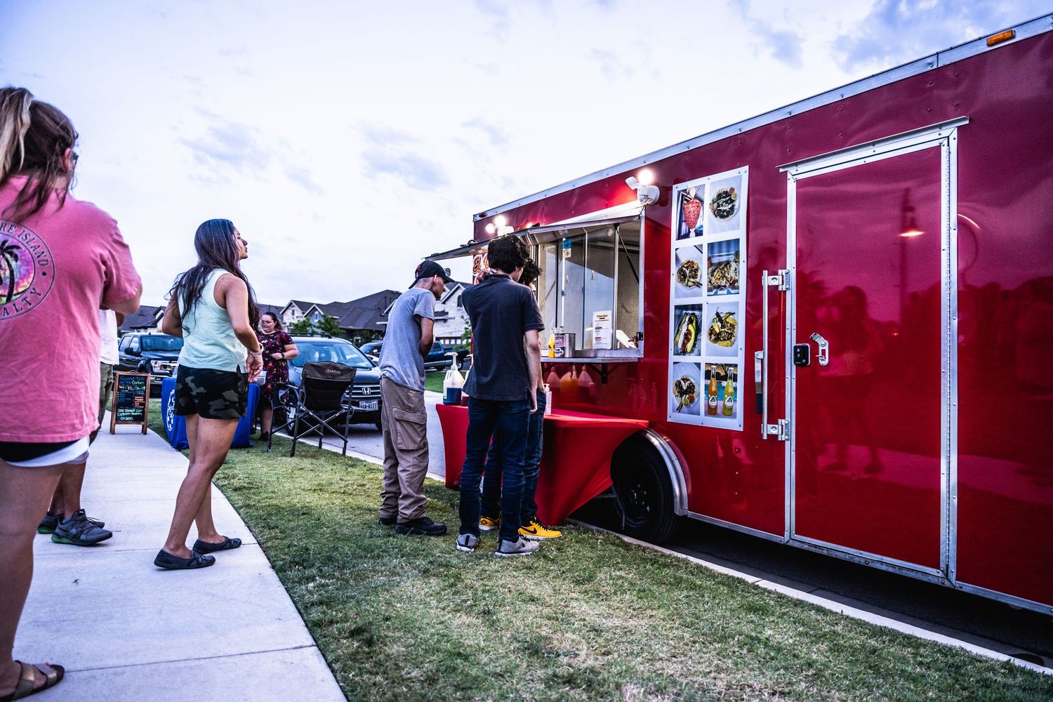 Red food truck serving customers at outdoor community event.