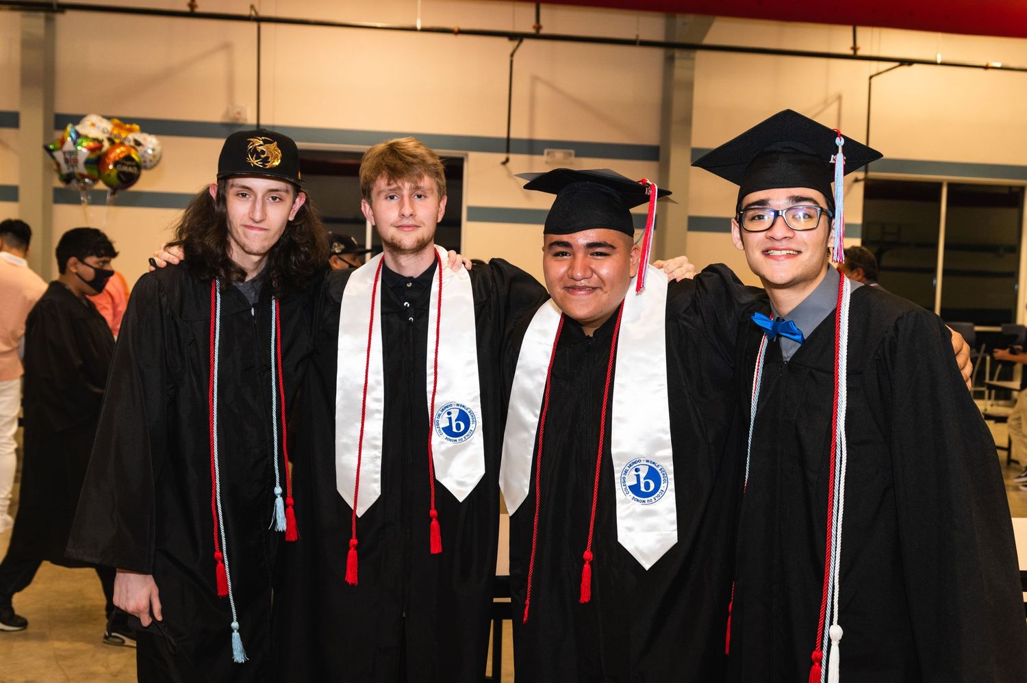Graduates in black caps and gowns with red stoles pose together during graduation ceremony.