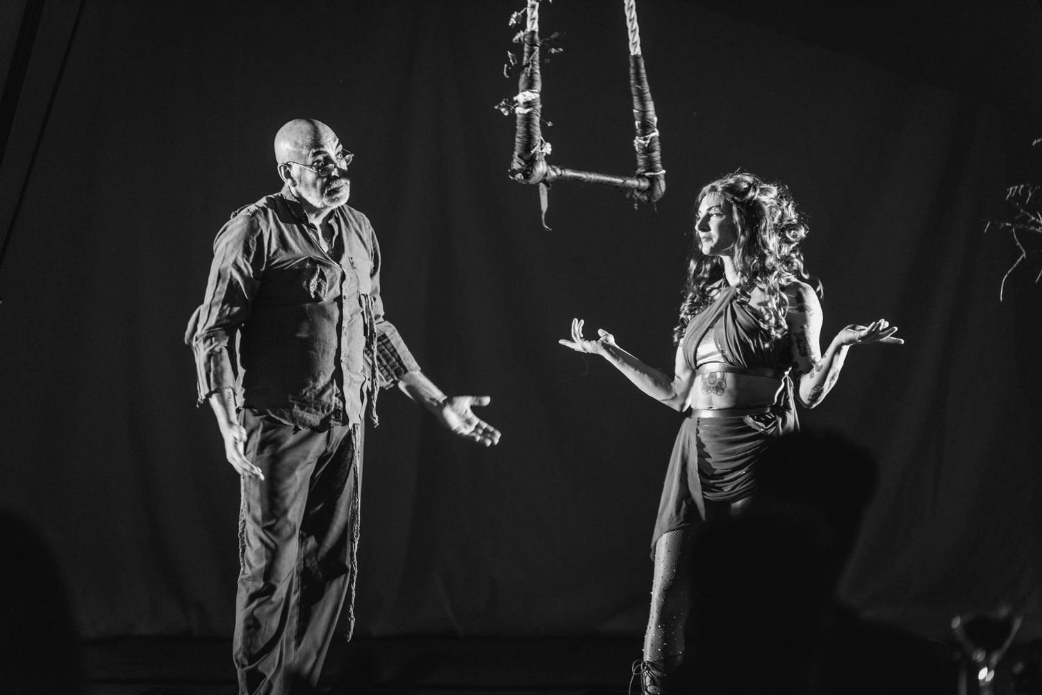 Two performers engage in dramatic dialogue on darkened stage during theatrical performance.