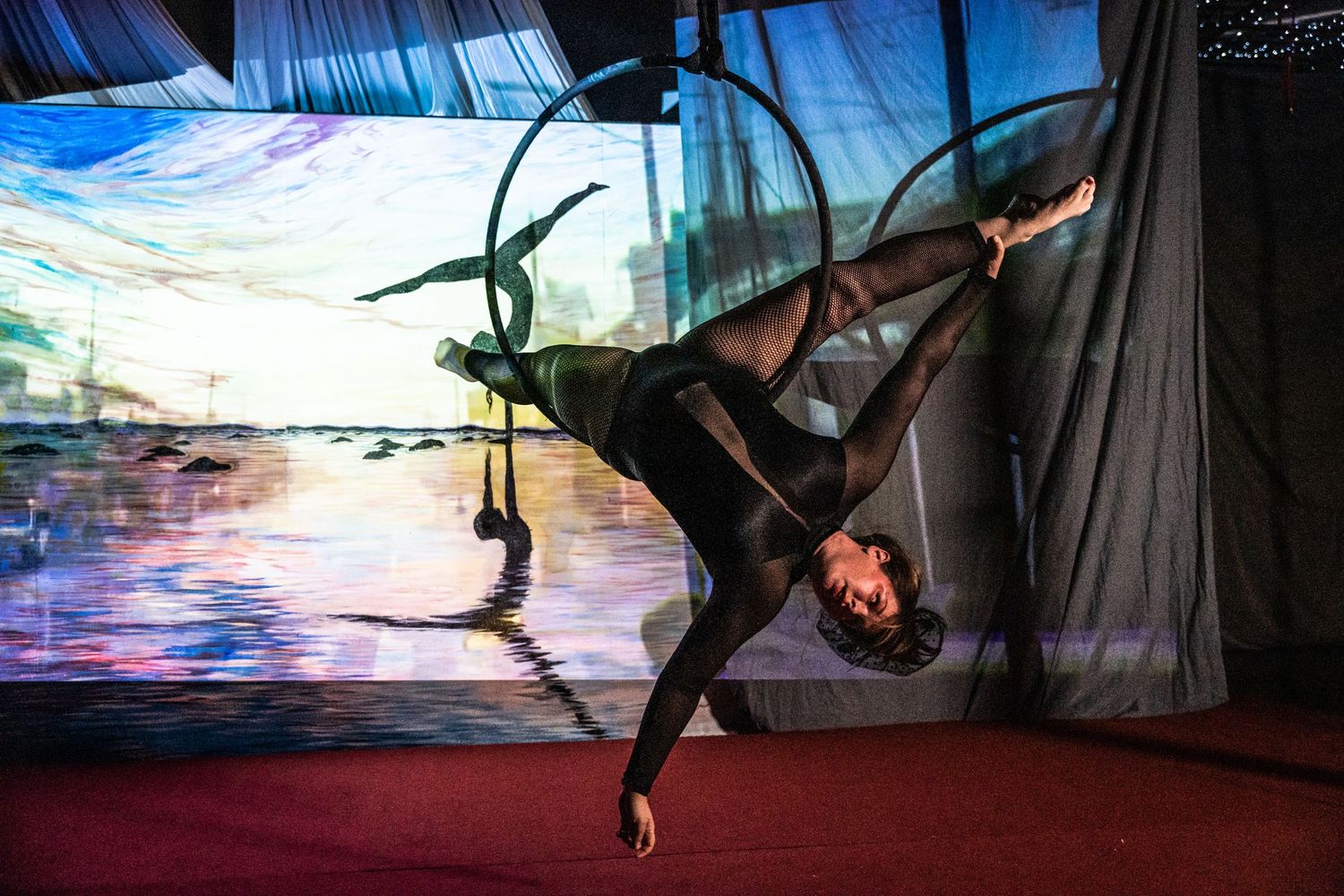 An aerial performer in black attire poses dramatically against a colorful projected background.