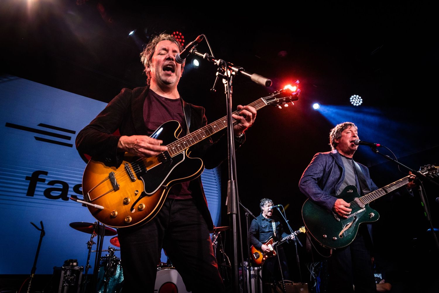 Musicians performing on stage with electric guitars under dramatic concert lighting.