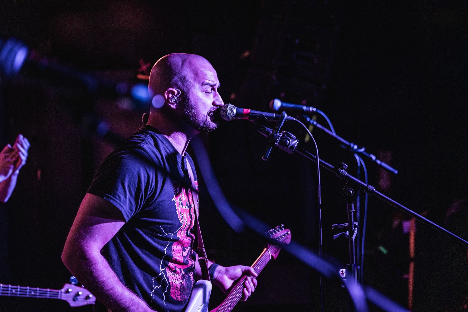 Musician performs on stage with guitar and microphone under blue stage lighting.