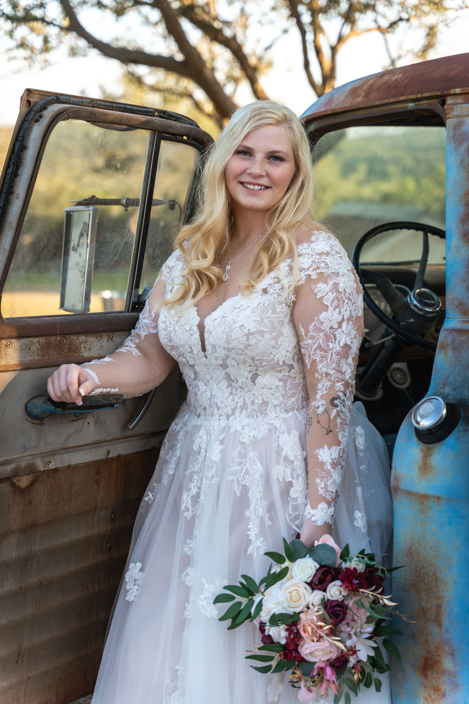 Beautiful wedding portrait with vintage blue pickup truck in rustic outdoor setting.