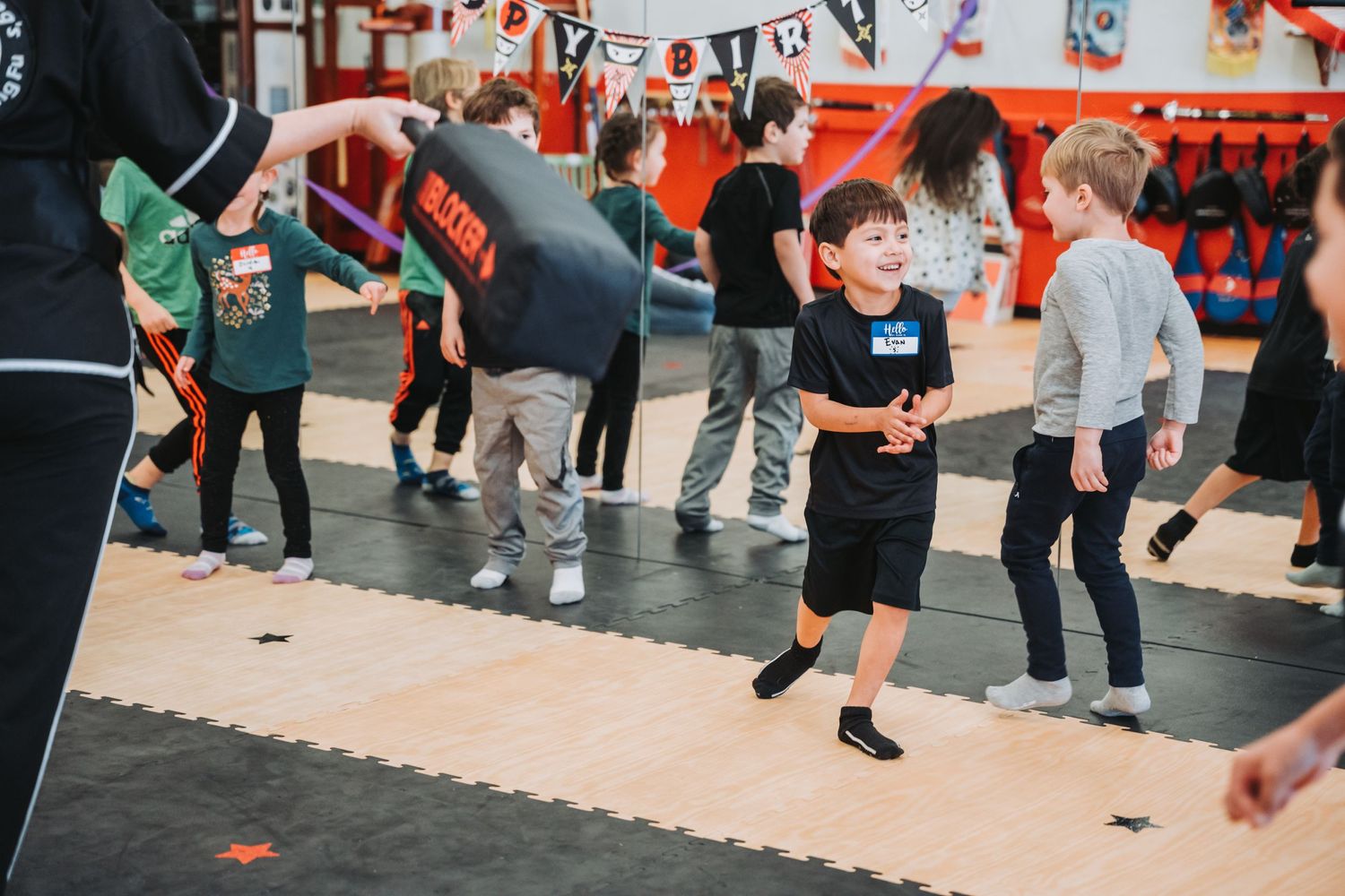 Young students practicing martial arts moves on interlocking foam mats in a training studio.