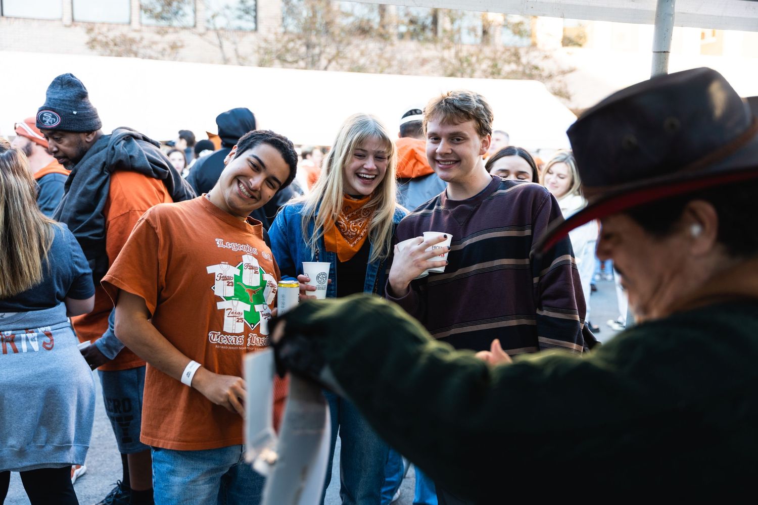 A crowd of fans in orange and blue gather around a table at an outdoor event.
