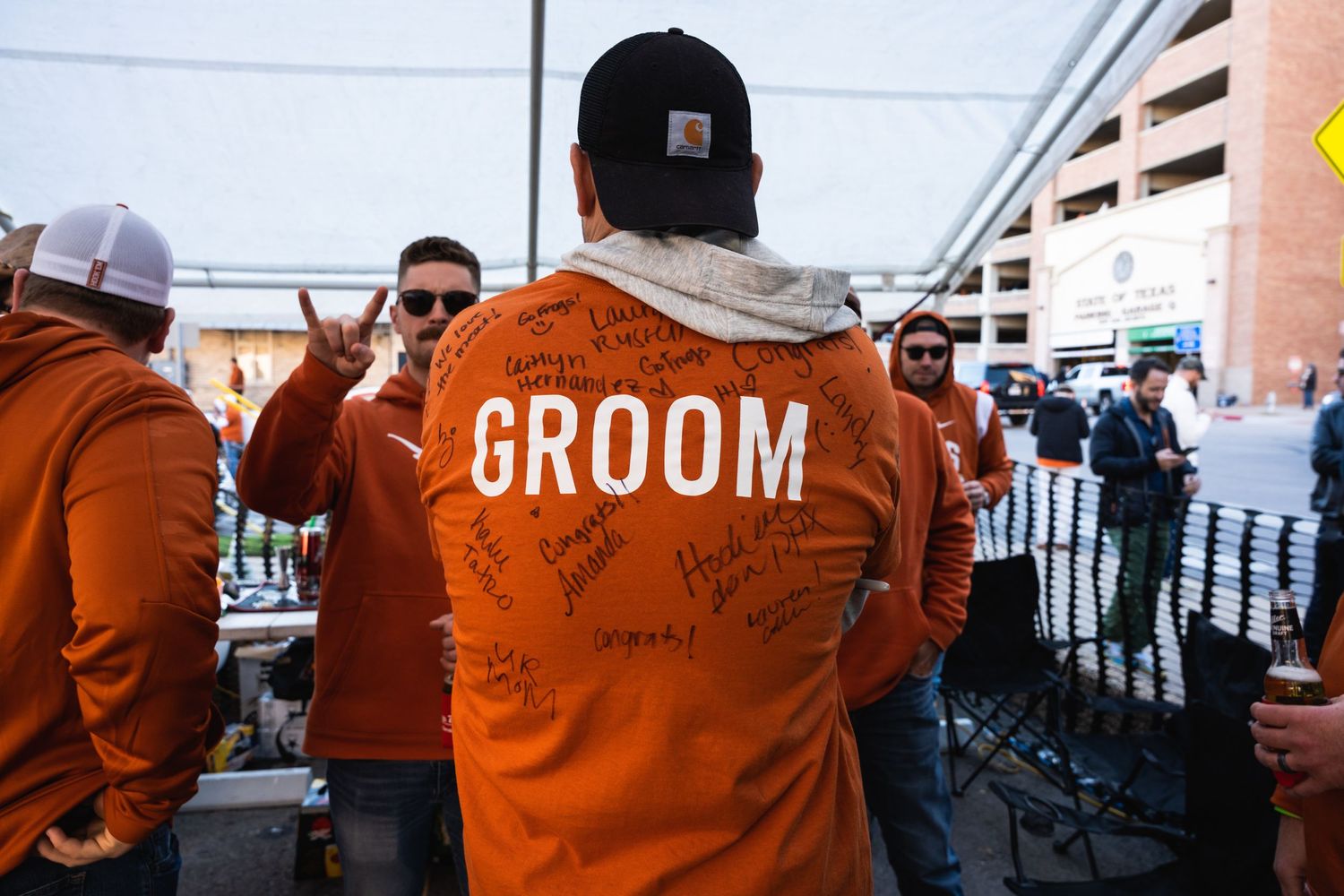 Back view of someone wearing an orange jacket with 'GROOM' written on it at an outdoor event.