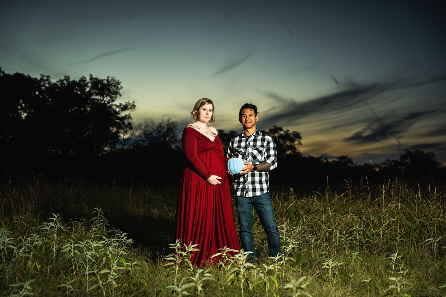 Sunset maternity photo with couple standing in wildflower field.