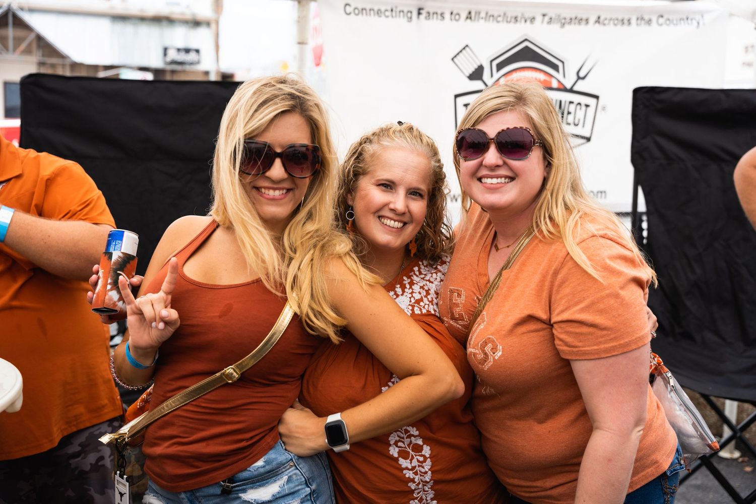 Three people in orange outfits pose together at a tailgate party.