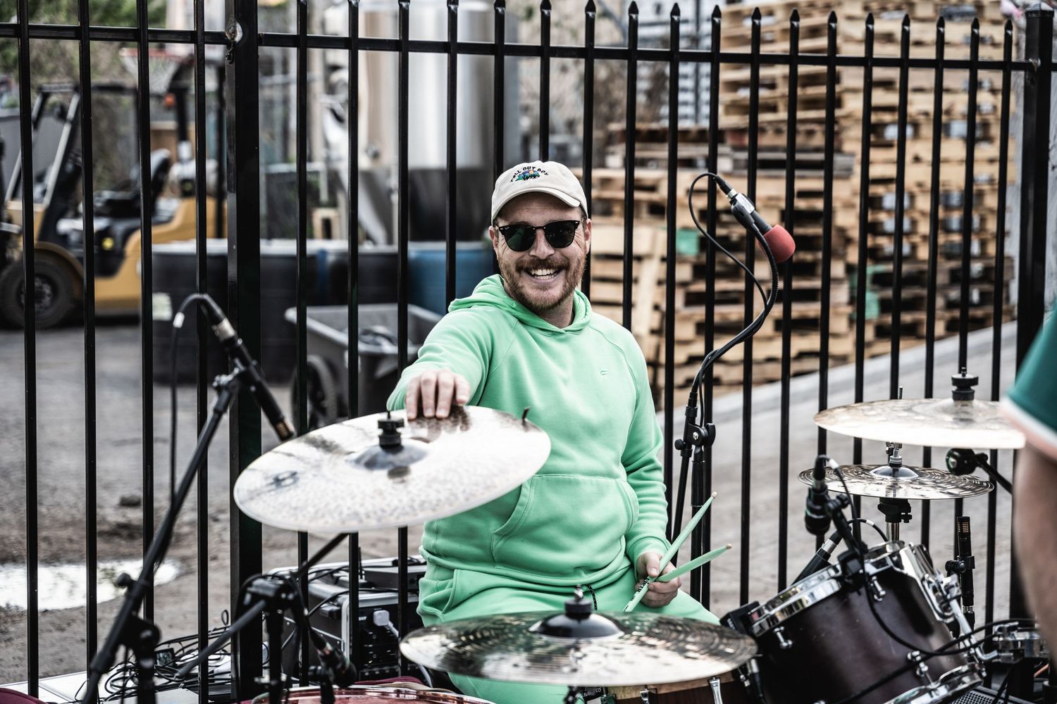 Drummer in mint hoodie and cap plays outdoor set with drum kit.