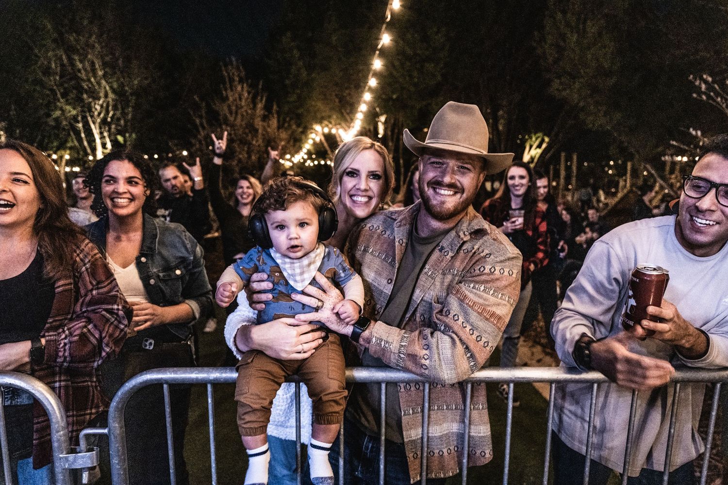Happy crowd enjoys nighttime outdoor concert under string lights.