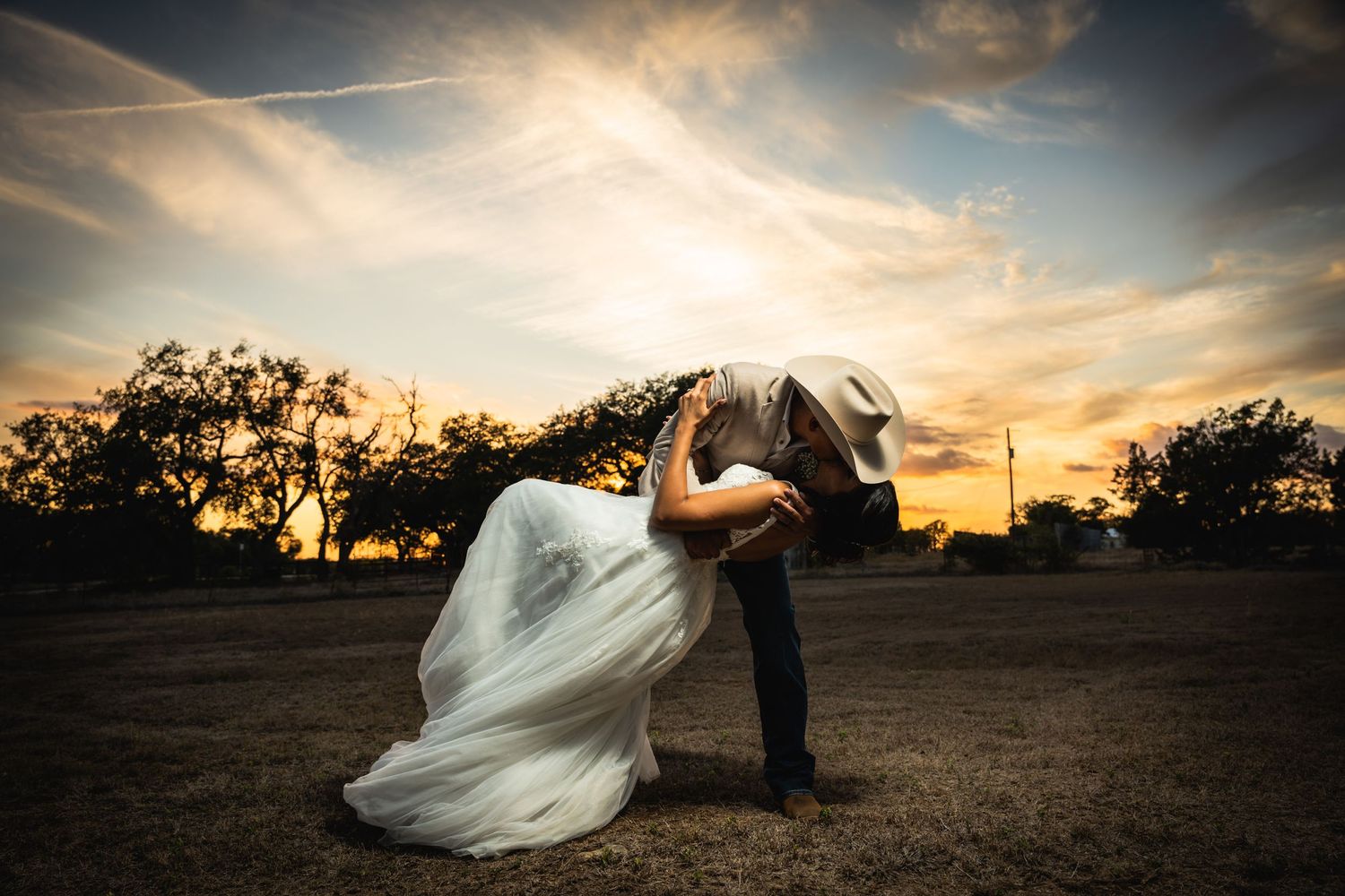 Dramatic dip pose with flowing white dress against a sunset sky.