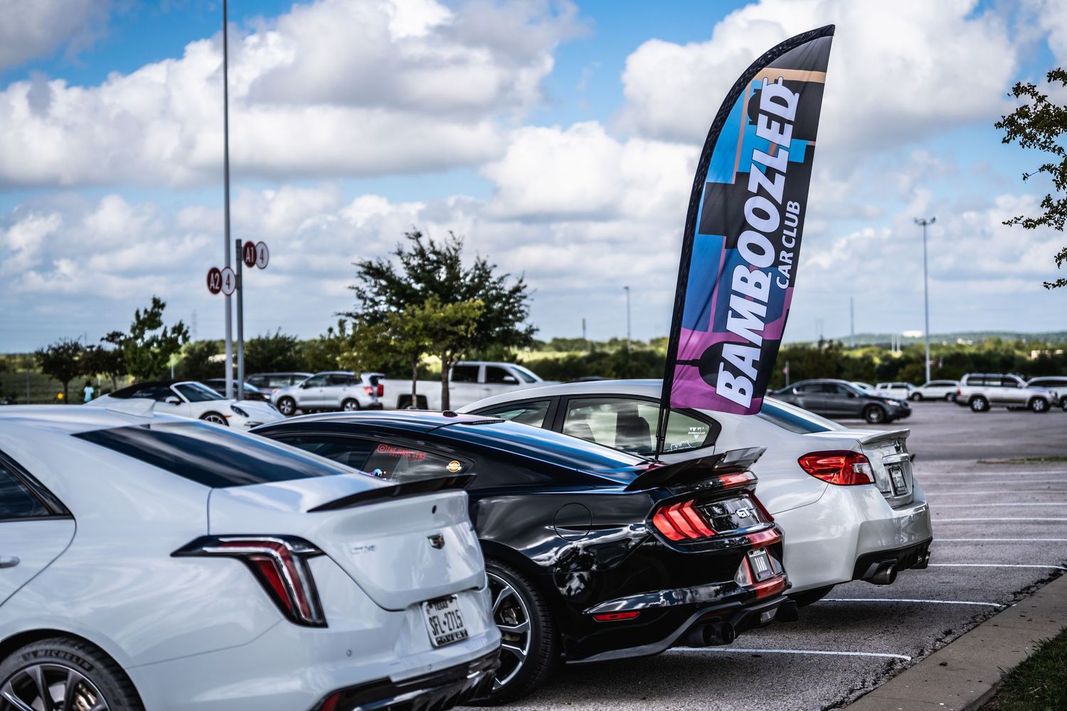 Row of modern sports cars parked under cloudy sky with racing banner flag.
