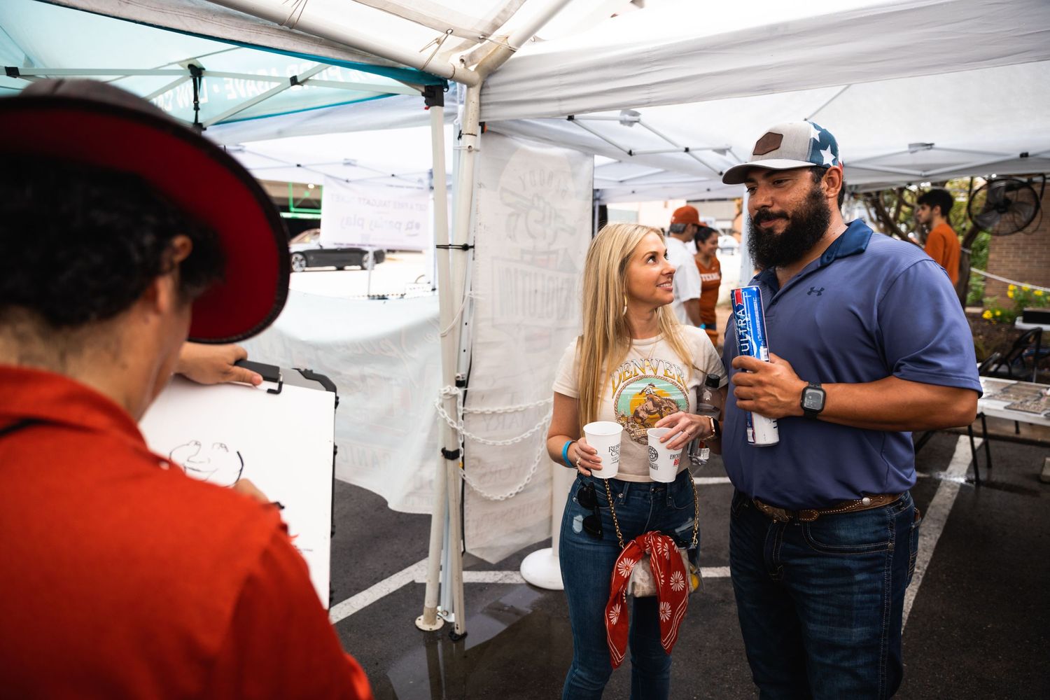 Customers interacting with a vendor at an outdoor market stall under a white tent.