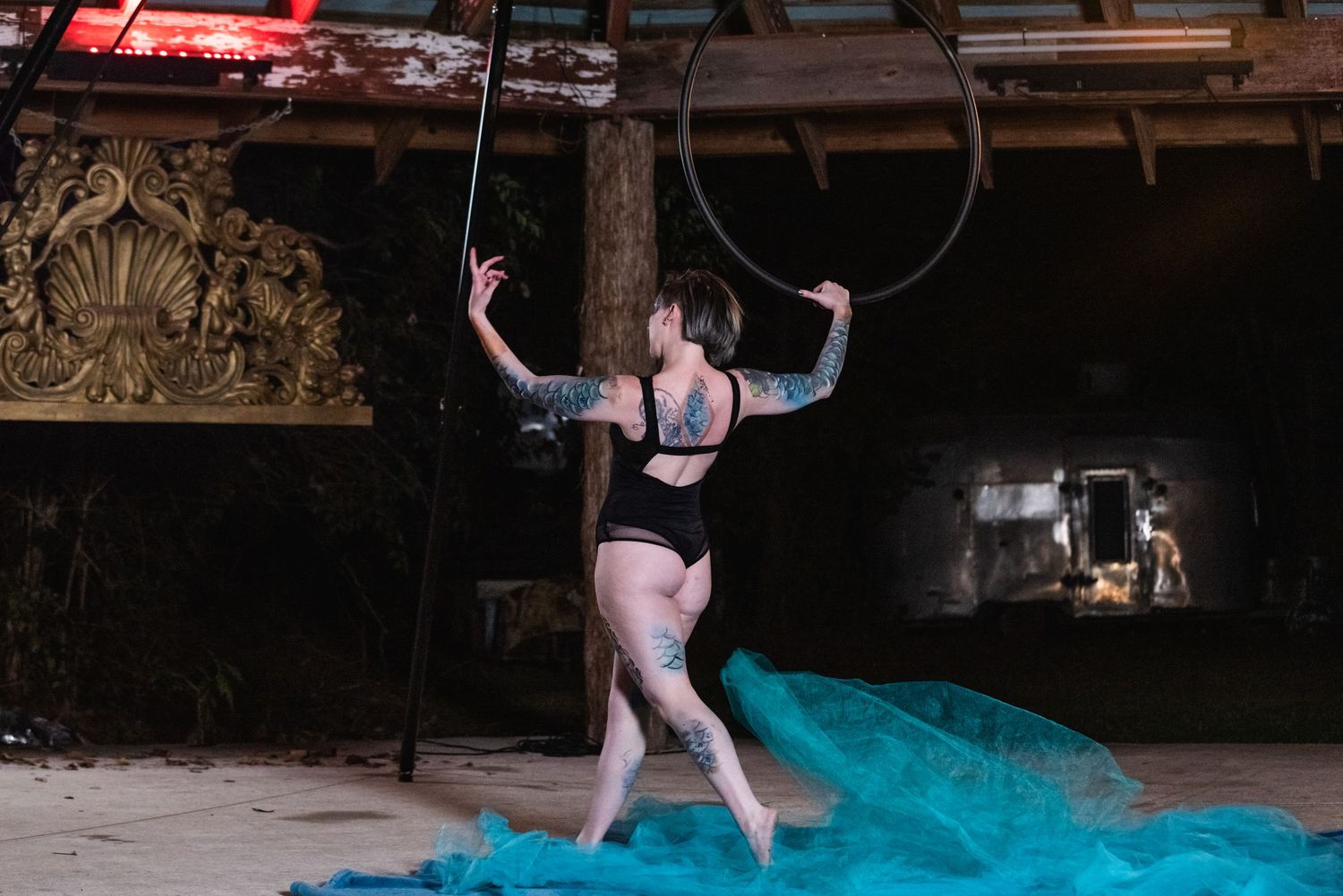 Aerial artist performs on suspended hoop over blue fabric in dimly lit venue.