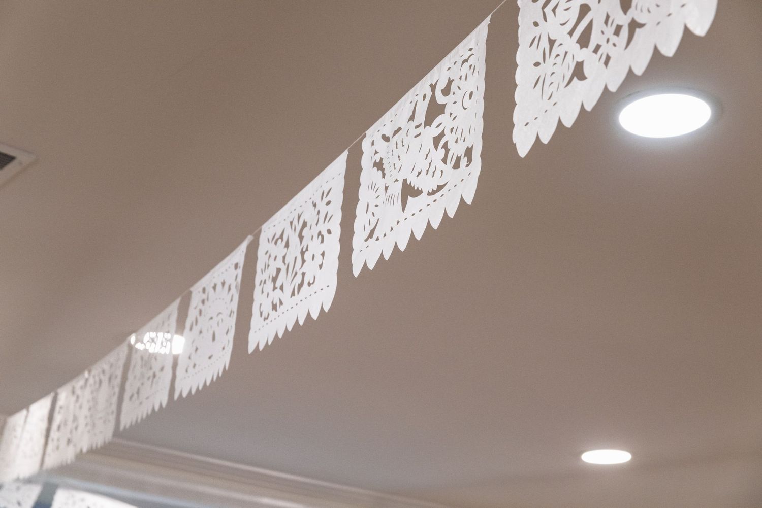 Decorative white papel picado banners hanging from a ceiling with recessed lighting.