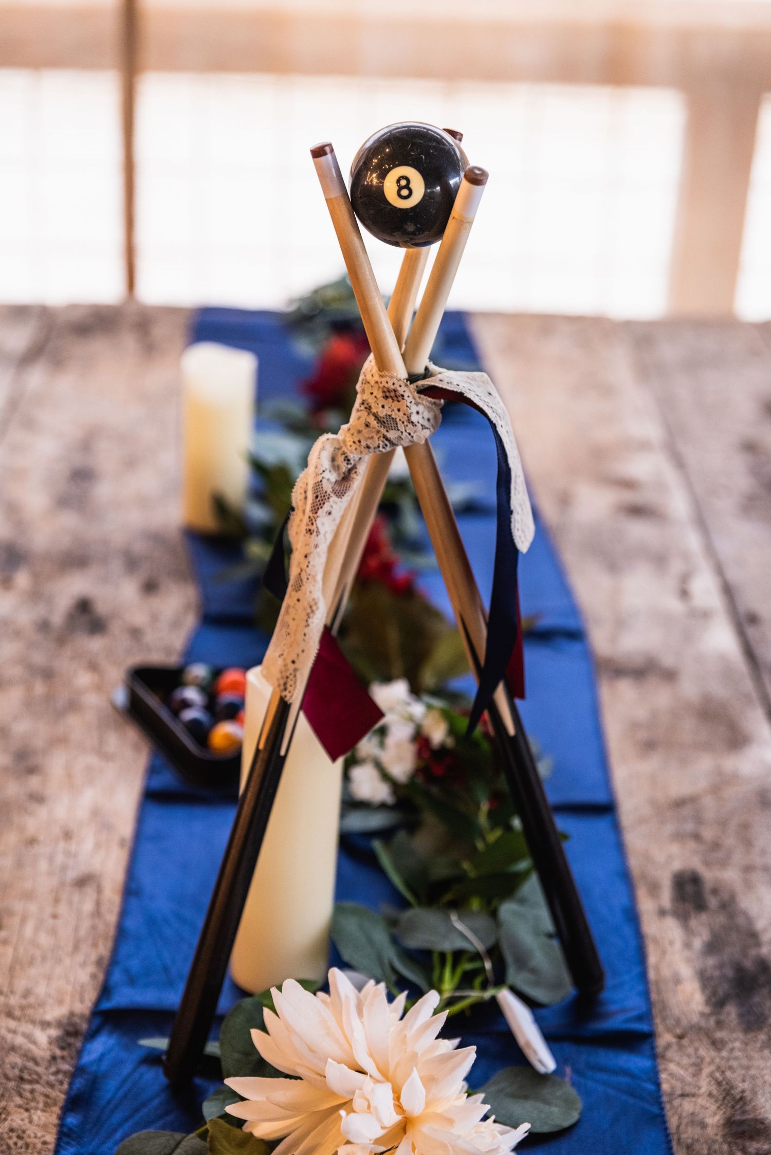 Crossed pool cues with an 8-ball displayed on a blue table runner with flowers.