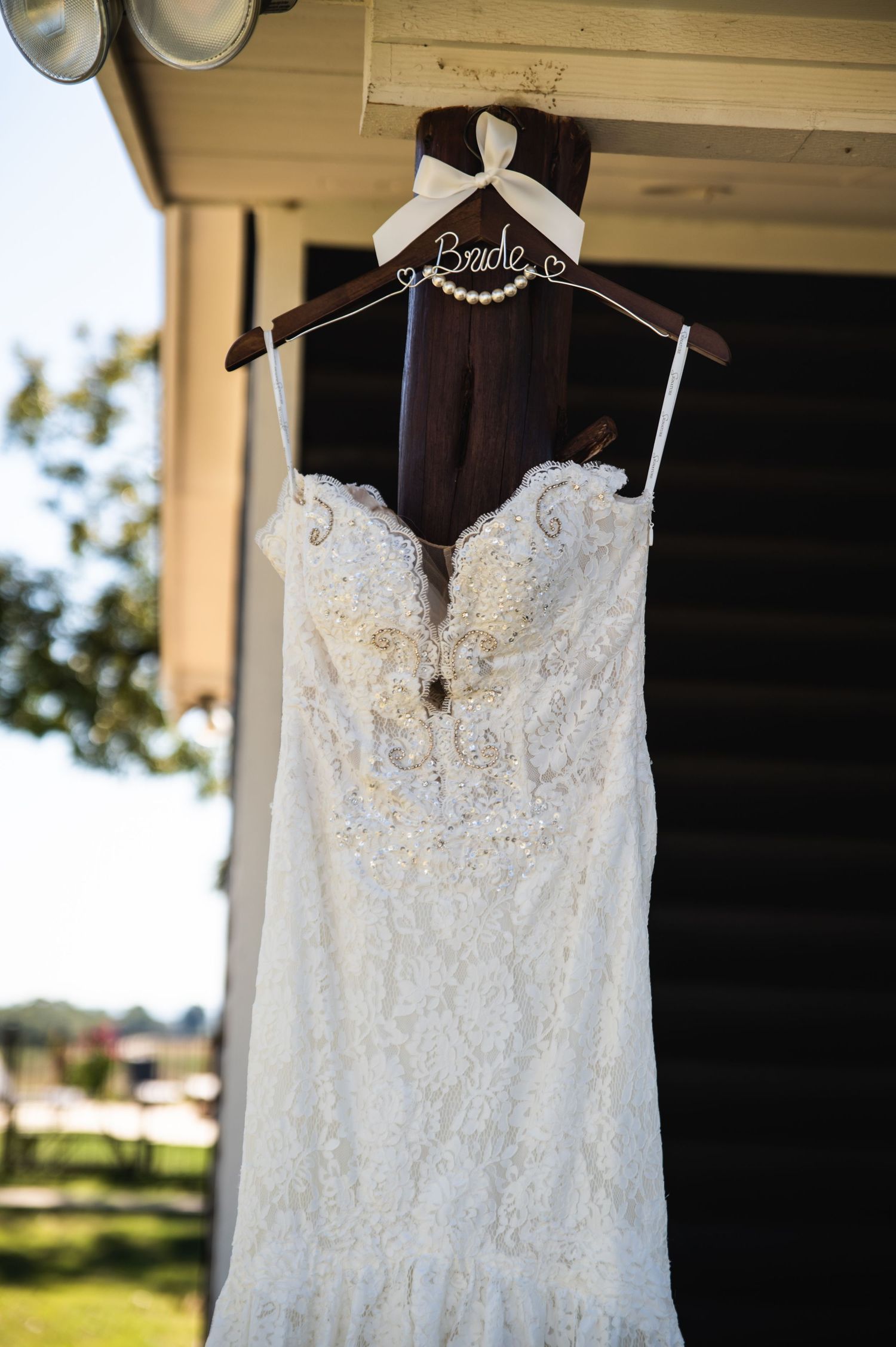 White lace wedding gown with sweetheart neckline displayed on wooden hanger against dark background.